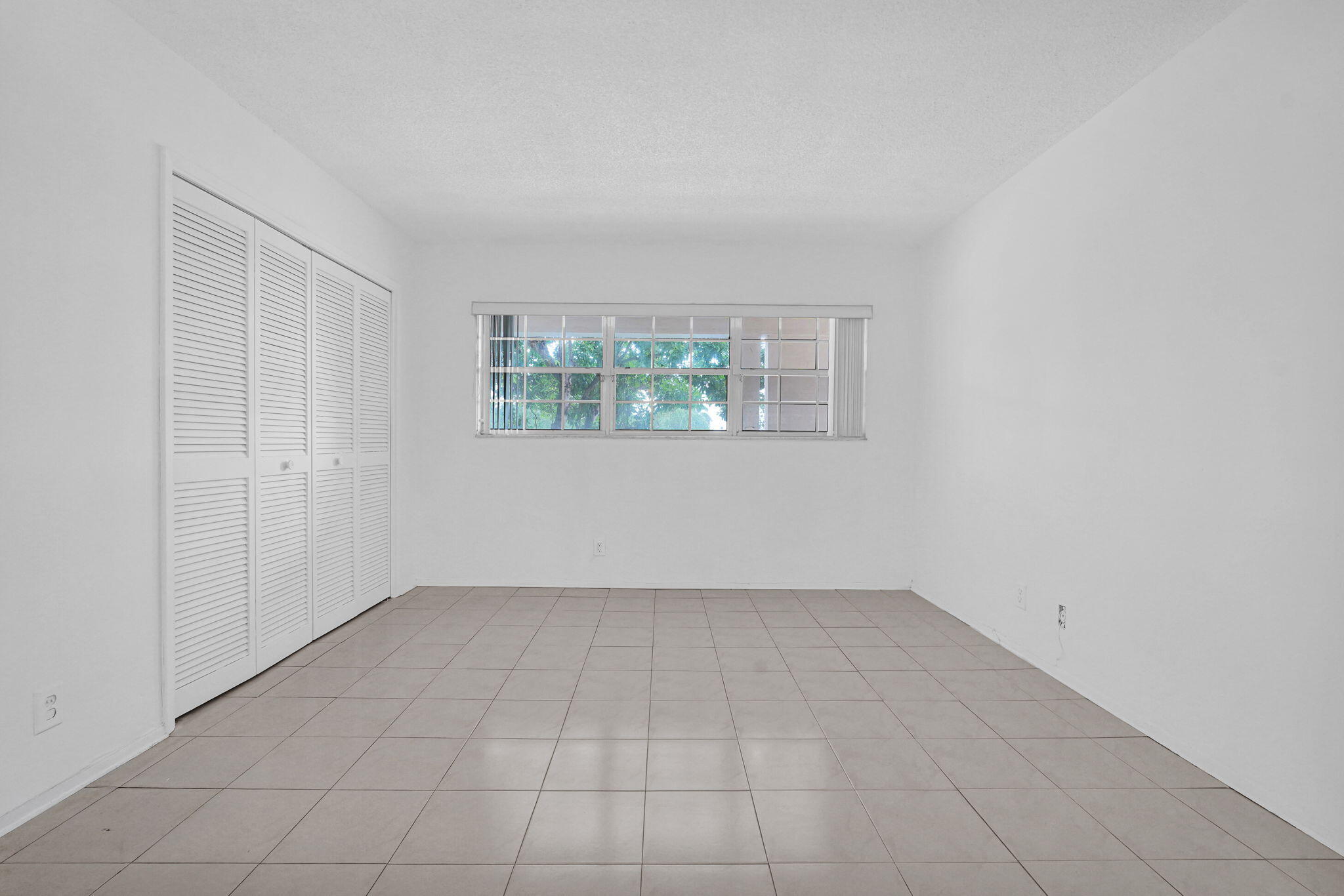 Room interior featuring neutral tile flooring, expansive wall space, and a multi-pane window with a horizontal blind