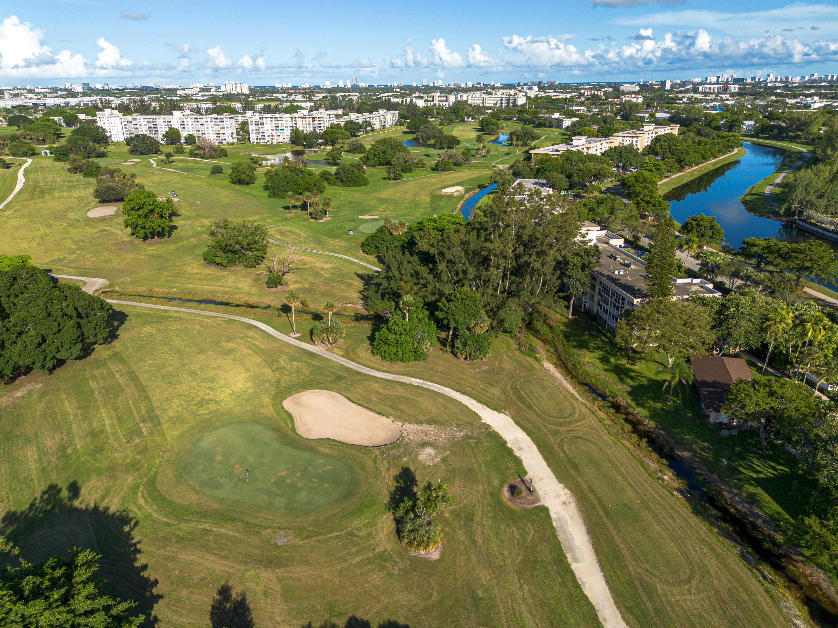 Aerial perspective of a golf course featuring manicured greens, sand bunkers, winding paths, mature trees, and a bordering waterway