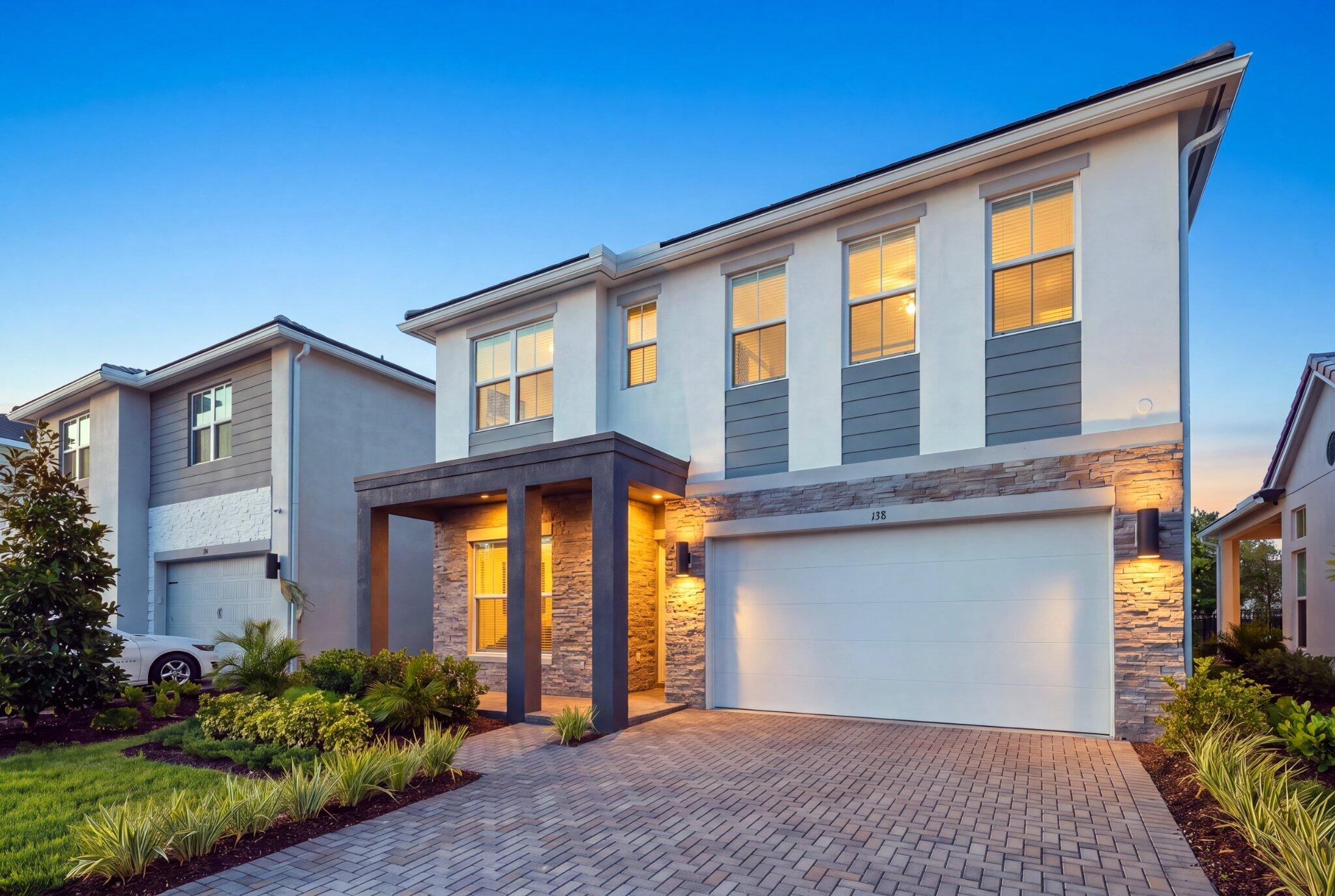 Two-story exterior featuring a stone-veneer facade, smooth-finish stucco, paver driveway, covered entryway, and multi-pane windows