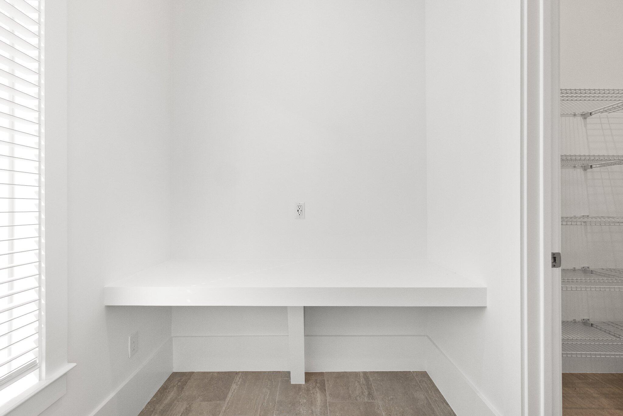Built-in desk with a crisp white finish, horizontal blinds, wood-finish flooring, and white wire shelving