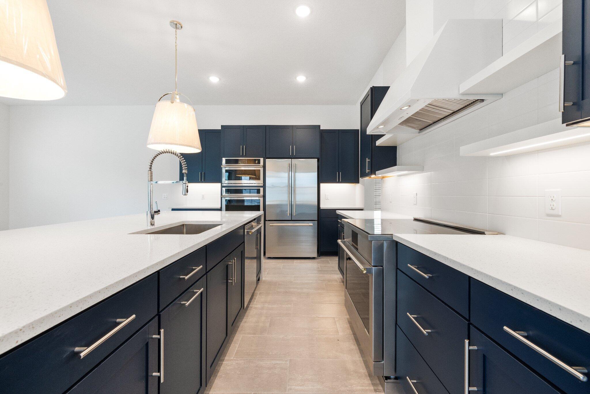 Kitchen featuring dark navy cabinetry, white quartz countertops, stainless steel appliances, a tile backsplash, and oversized pendant lighting