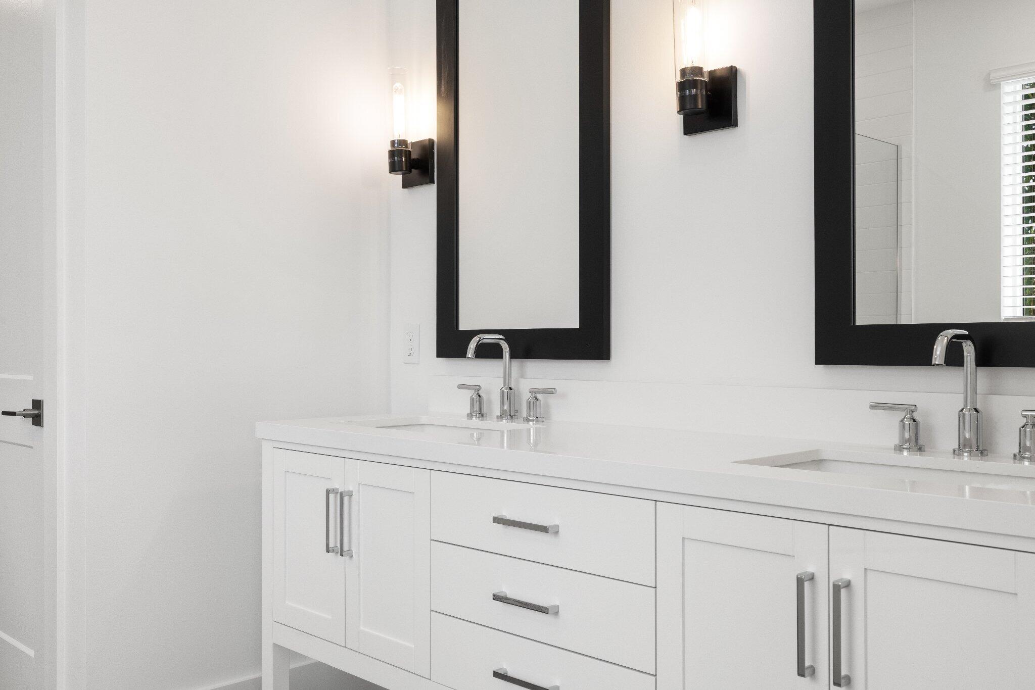 Dual-vanity cabinetry with white finish, solid surface countertop, chrome dual-handle faucets, and rectangular wall-mounted mirrors with black frames