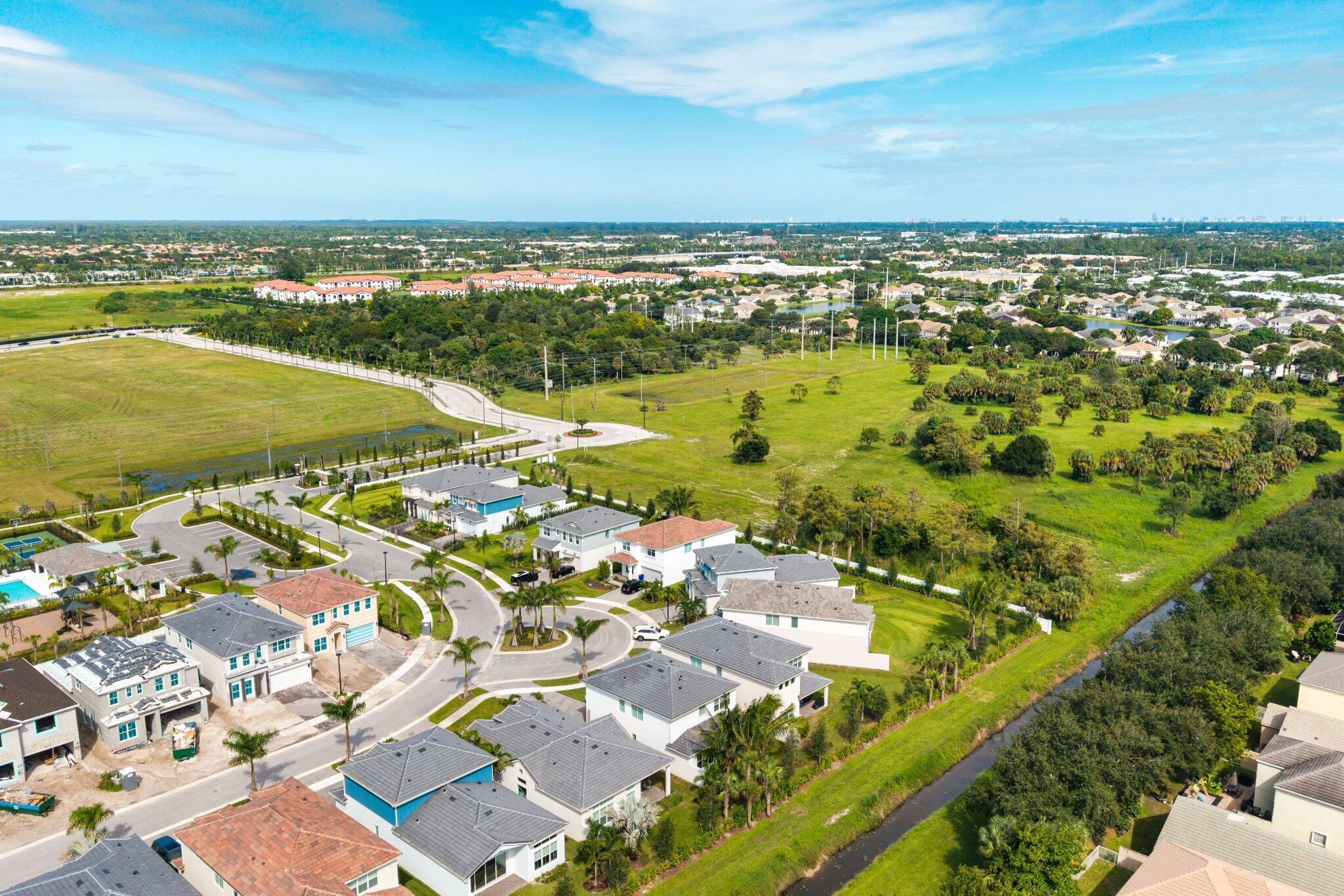 Aerial perspective featuring multi-story residential structures with tile roofing, paved cul-de-sac streets, established landscaping with palms, and expansive surrounding green space