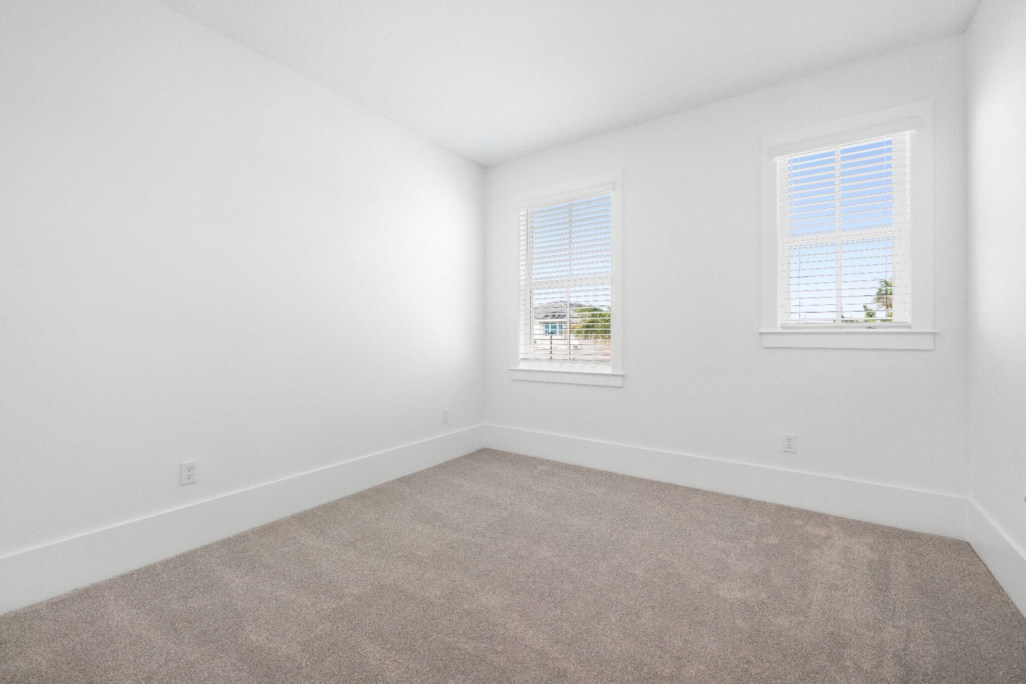Neutral-toned carpet flooring, crisp white wall finish, and two double-hung windows with fixed horizontal blinds