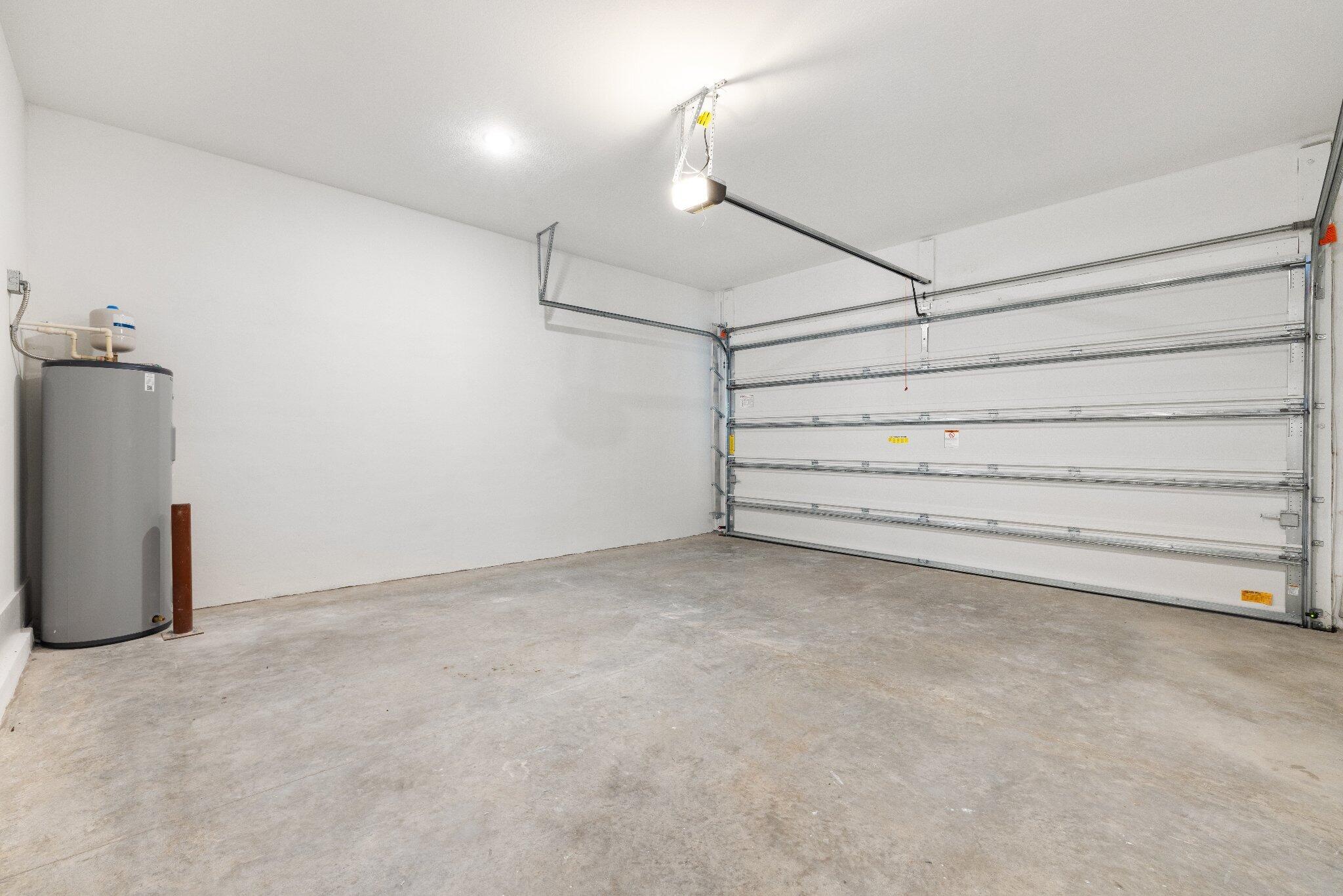 Enclosed garage space featuring a concrete floor, painted walls, an overhead sectional door, and an integrated water heater