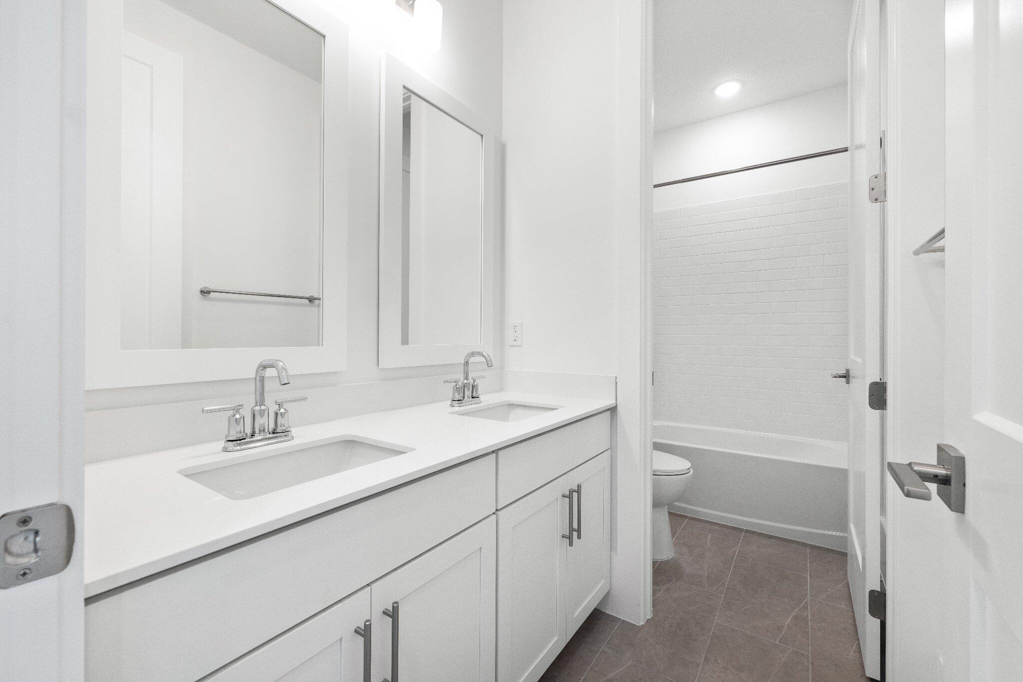 Dual-sink vanity with white shaker-style cabinetry, solid-surface countertop, rectangular undermount basins, and framed wall mirrors