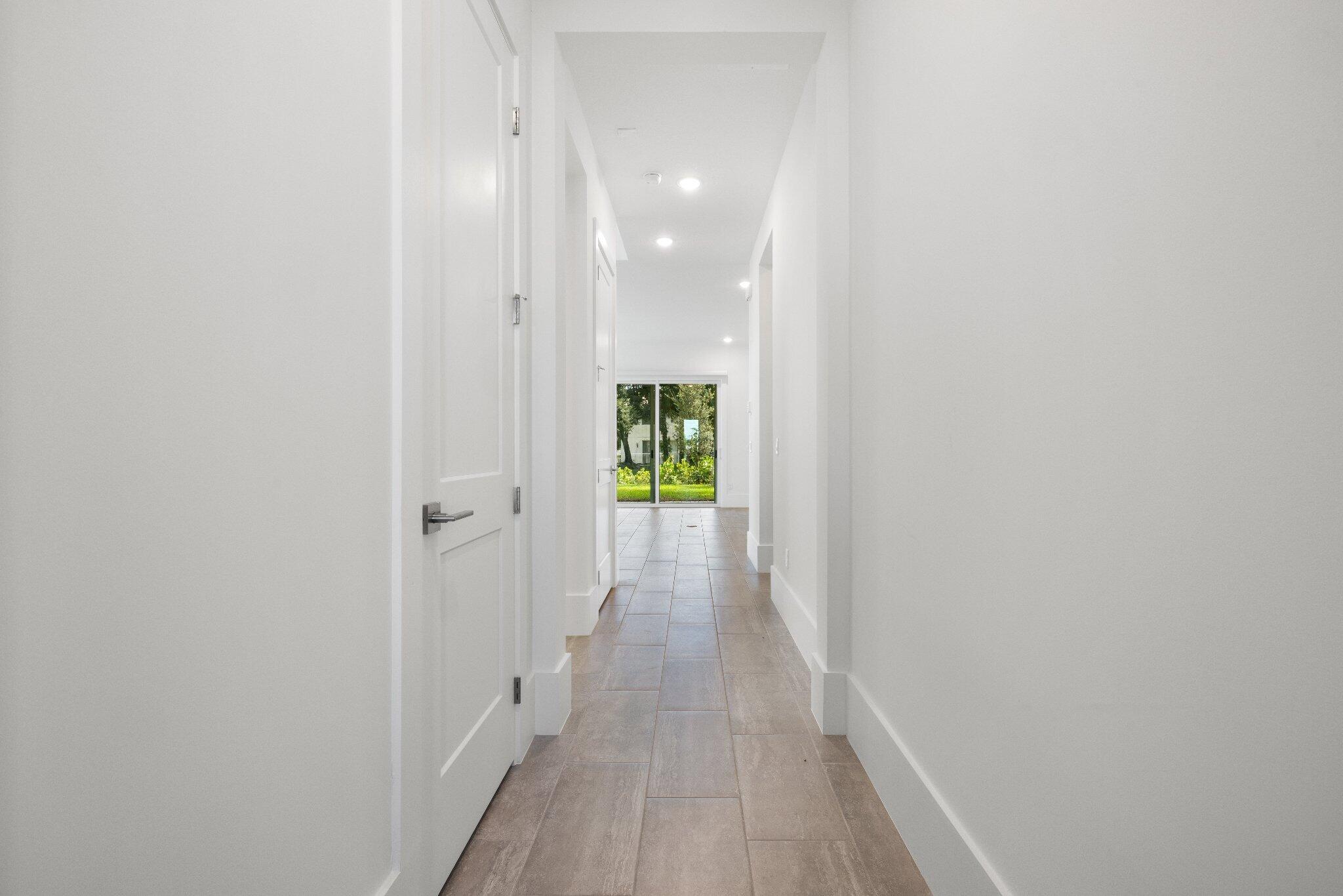 Hallway featuring wood-finish flooring, white paneled doors, recessed ceiling lighting, and sliding glass doors