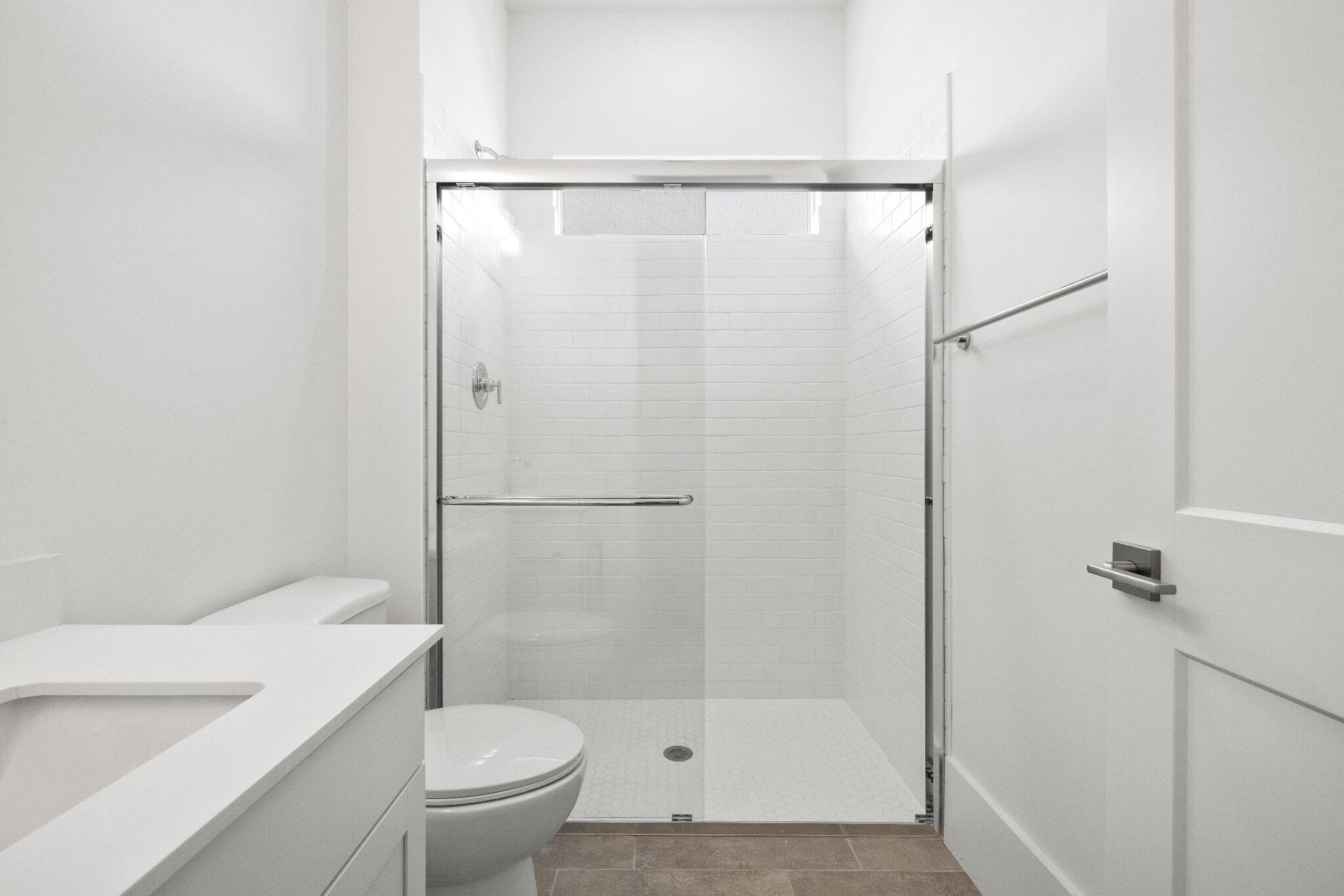 Bathroom featuring a glass-enclosed shower with white tiled walls, a vanity with a white countertop, and neutral-toned floor tile