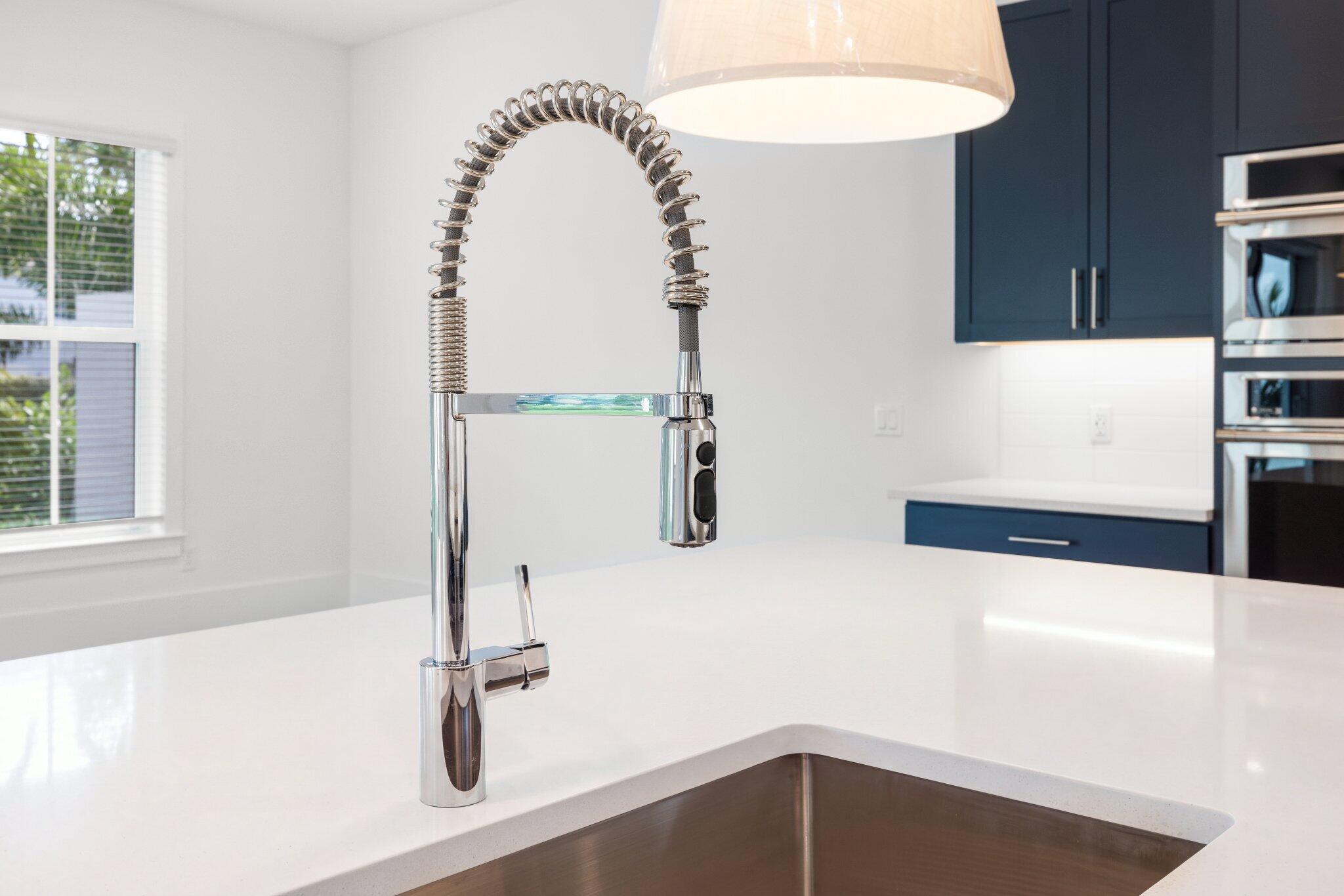 Quartz countertop with undermount stainless steel sink, professional-style high-arc spring faucet, navy blue cabinetry, and built-in wall oven