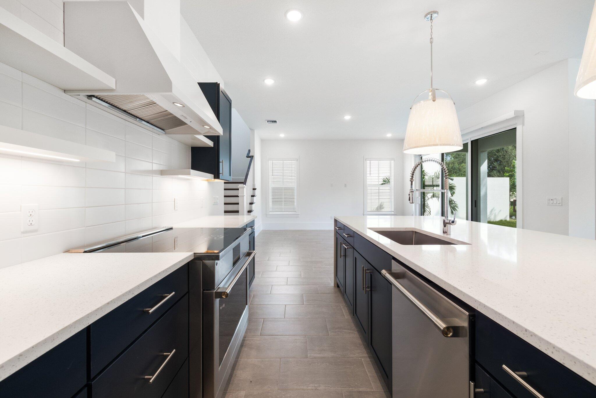 Kitchen featuring dark cabinetry, expansive quartz countertops, stainless steel appliances, white subway tile backsplash, and ceramic tile flooring