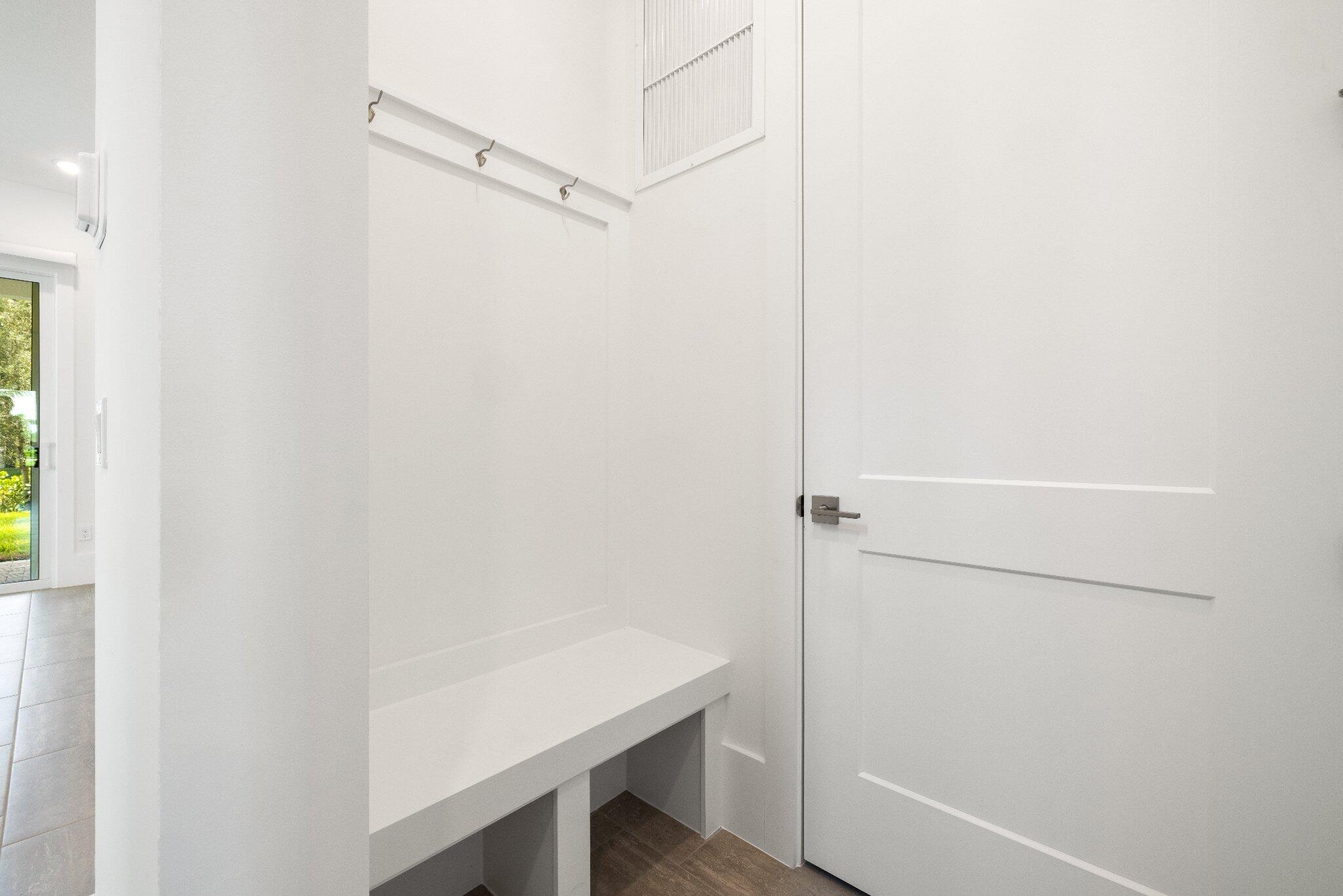 Built-in white storage bench featuring mounted wall hooks, a shaker-style interior door, and clean architectural lines