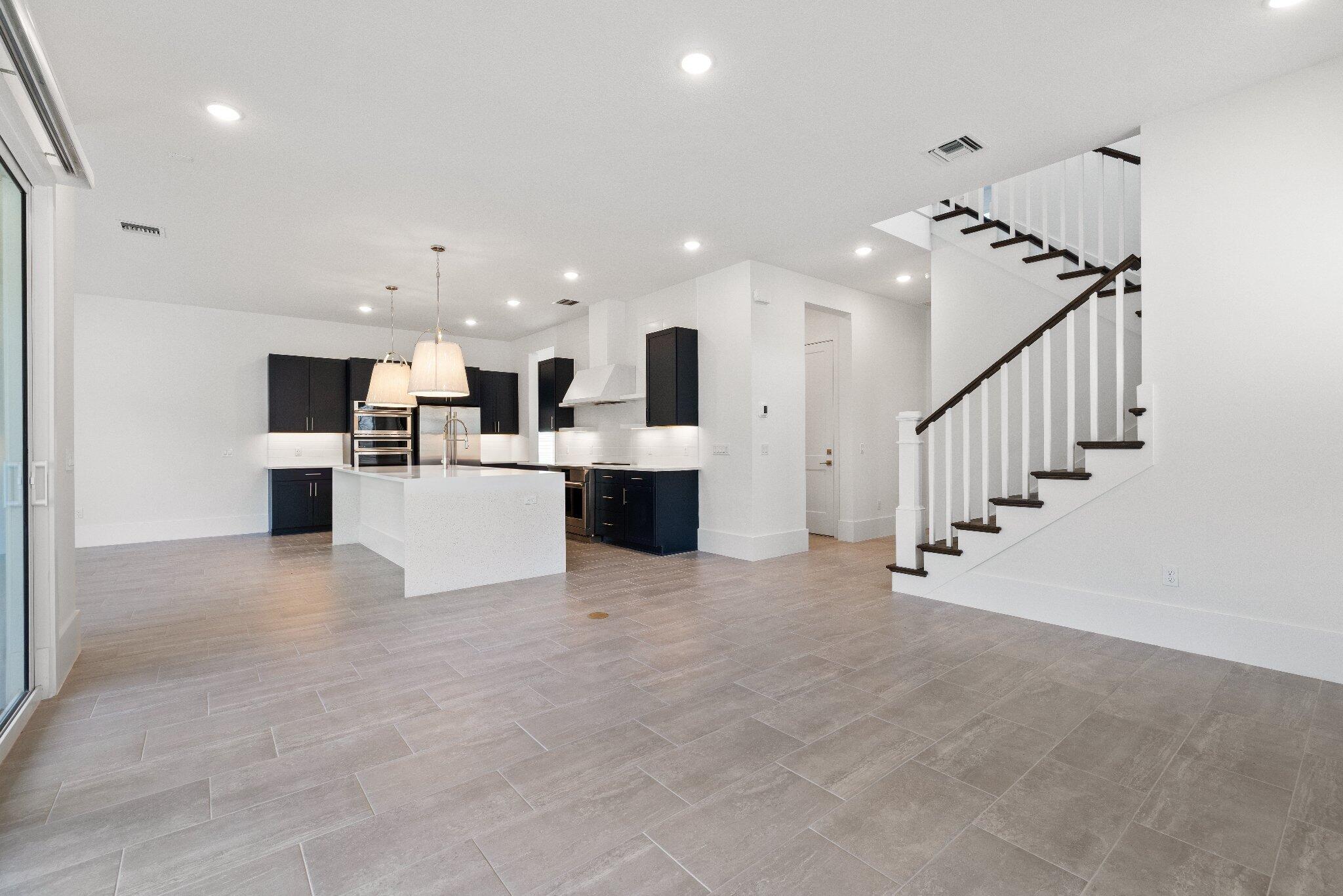 Open-concept interior featuring large-format tile flooring, recessed lighting, and a central kitchen island with a stone-surface countertop