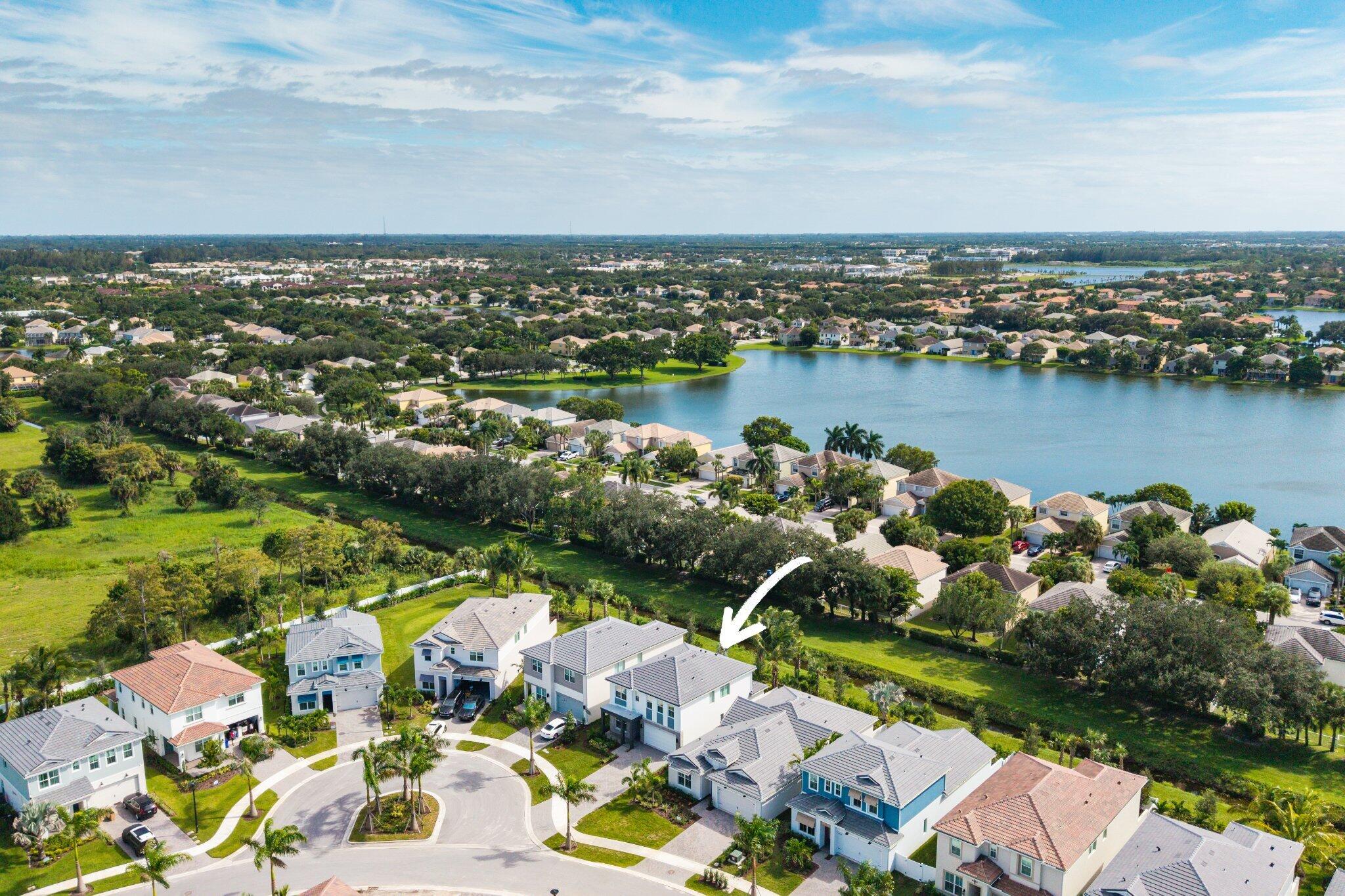 Aerial perspective of a two-story residence featuring a multi-pitched tiled roof, stucco exterior, attached garage, and a location backing onto a lake