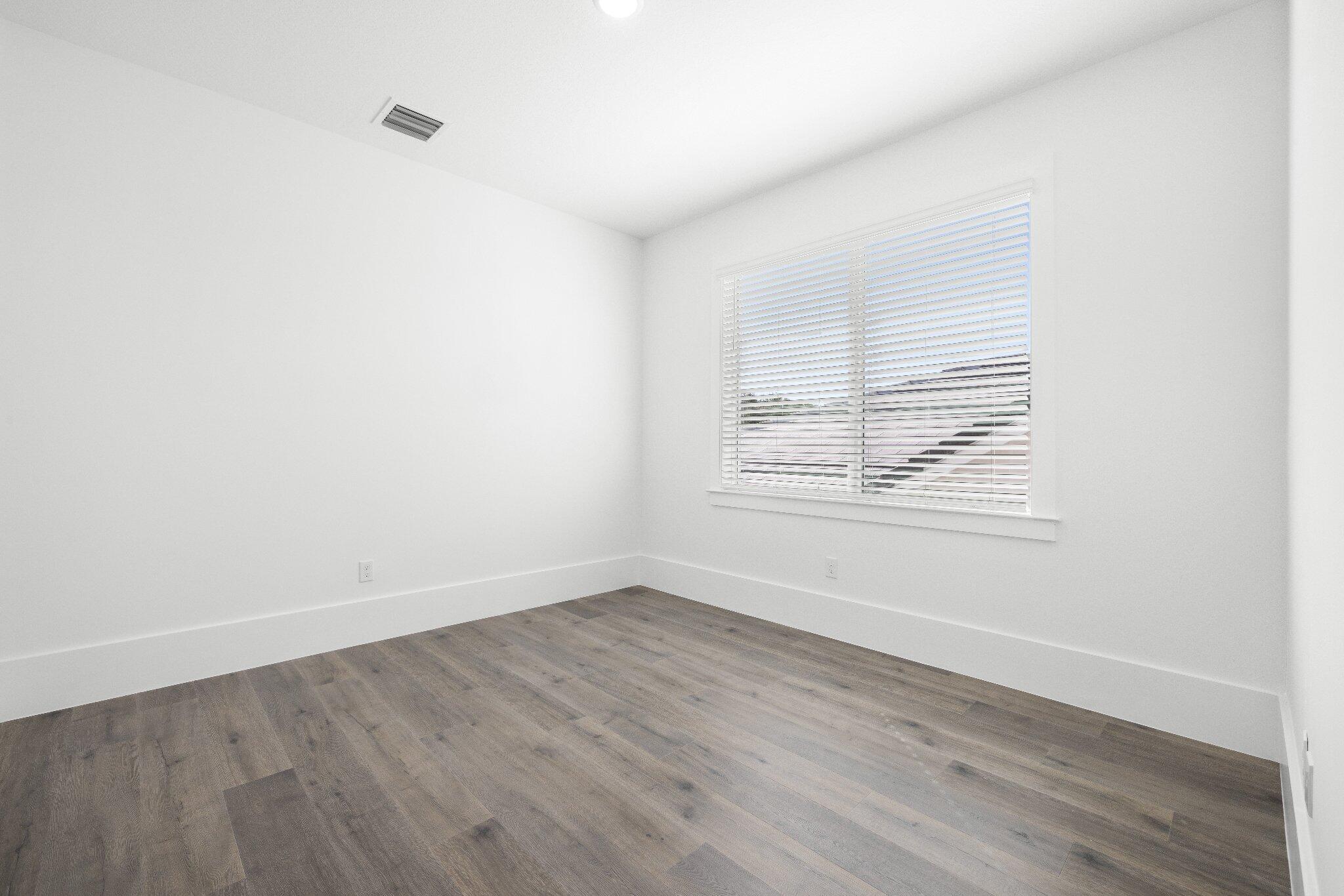 Neutral interior space featuring wood-finish flooring, white walls, and a large window with horizontal blinds