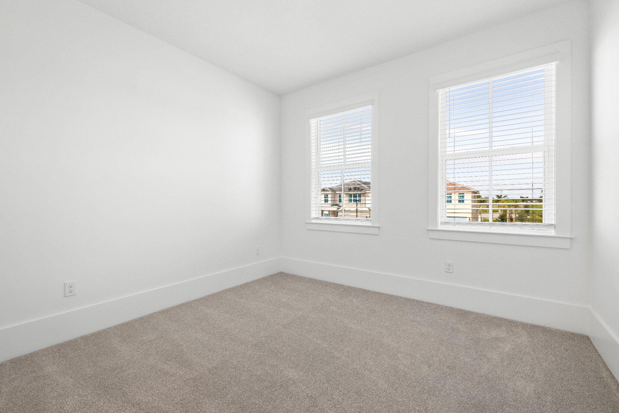 Neutral interior space featuring wall-to-wall carpeting, two double-hung windows with integrated blinds, and white wall finishes