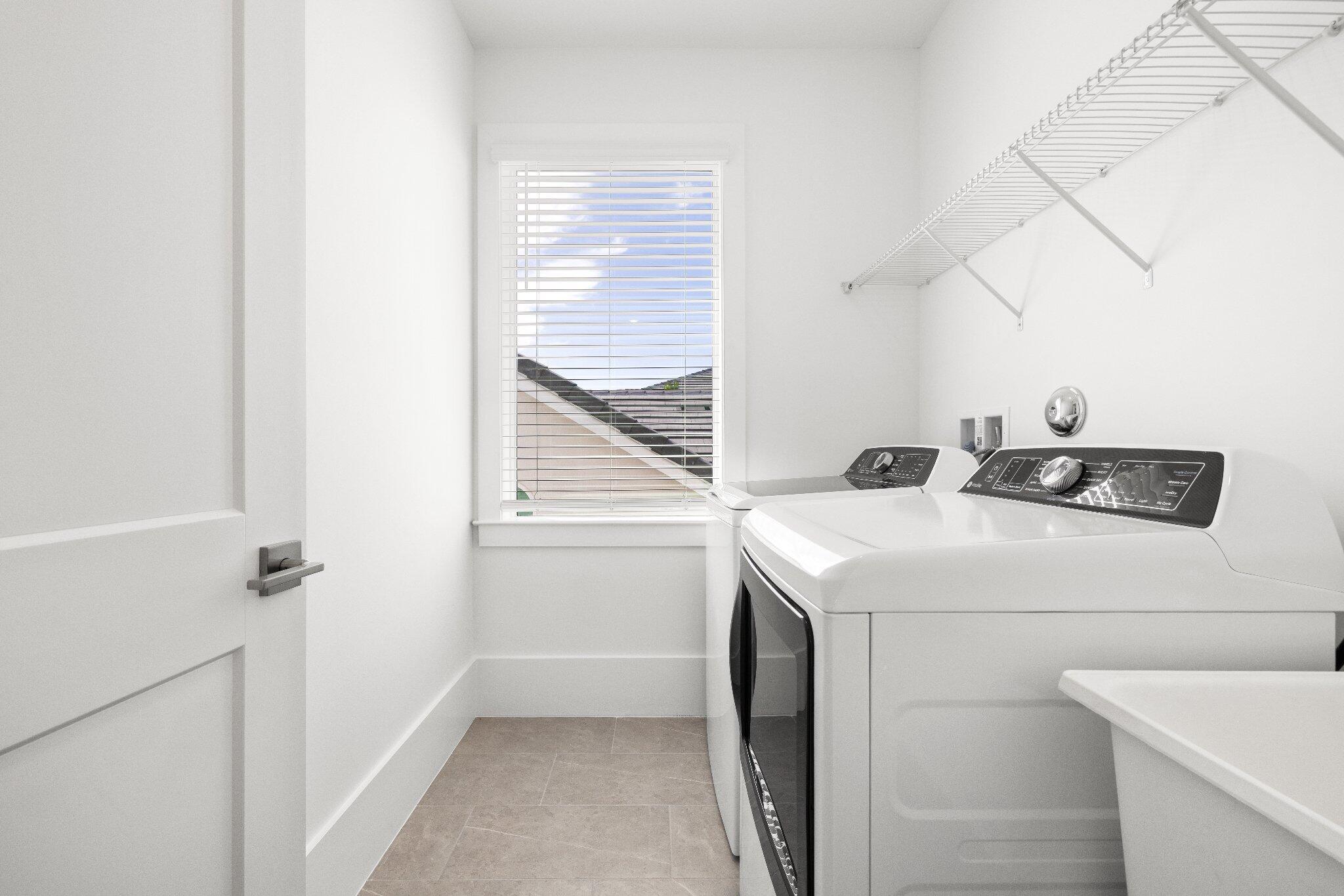 Utility room featuring a window with horizontal blinds, neutral tile flooring, and overhead wire shelving