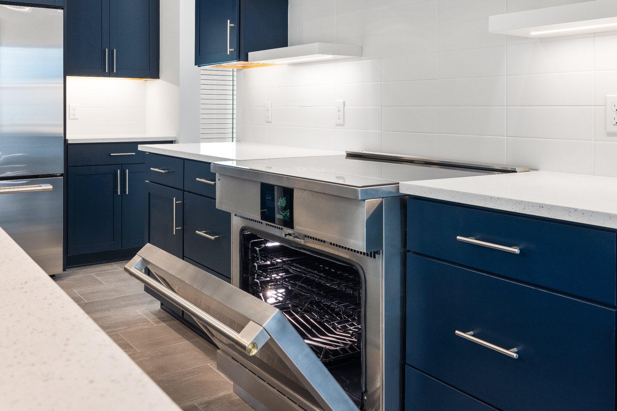 Kitchen featuring deep blue cabinetry, stainless steel slide-in range, white stone-composite countertops, and white tile backsplash