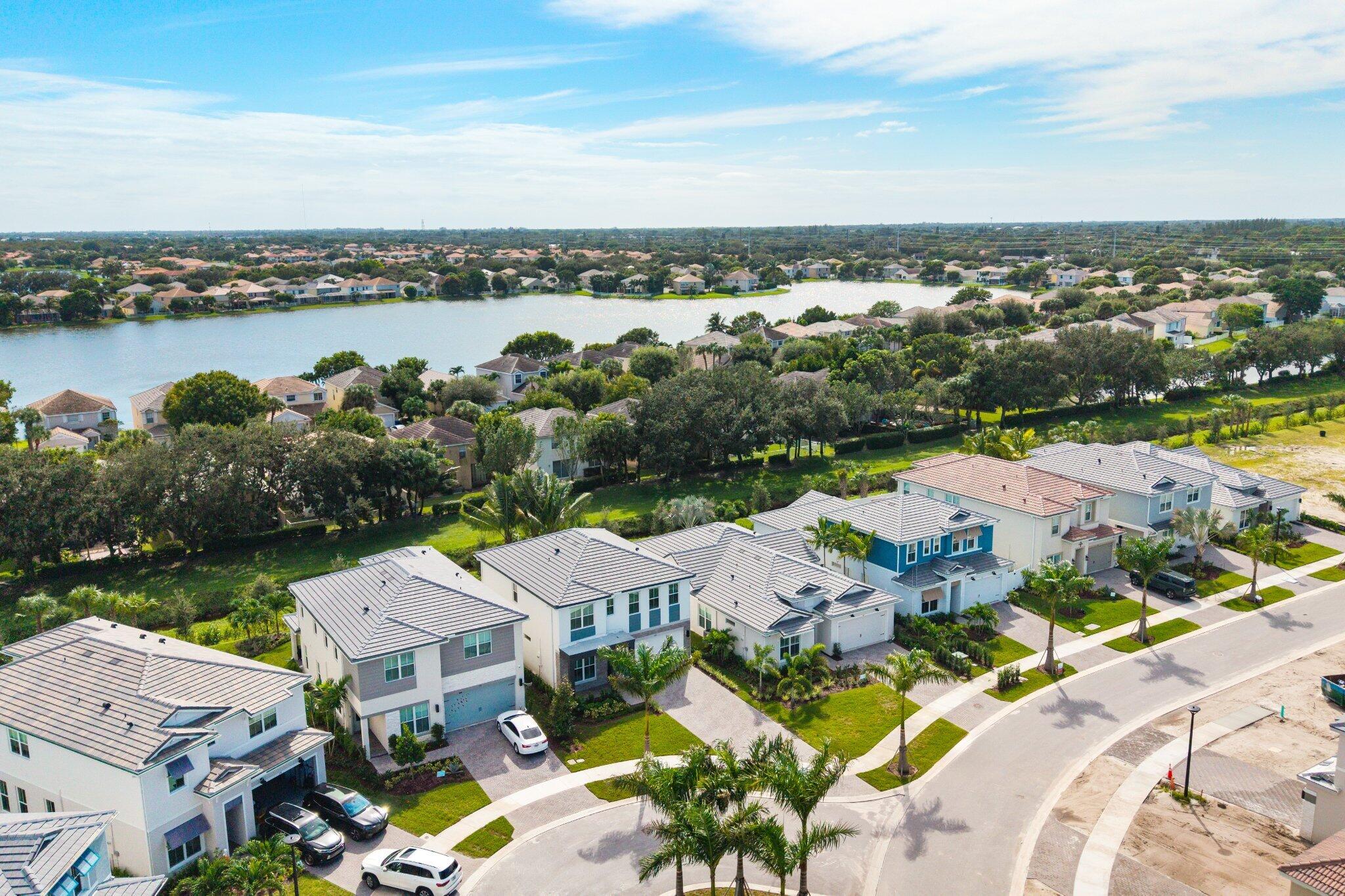 Aerial perspective featuring multi-story residential structures with tile roofing, paved driveways, manicured lawns, and proximity to a lake