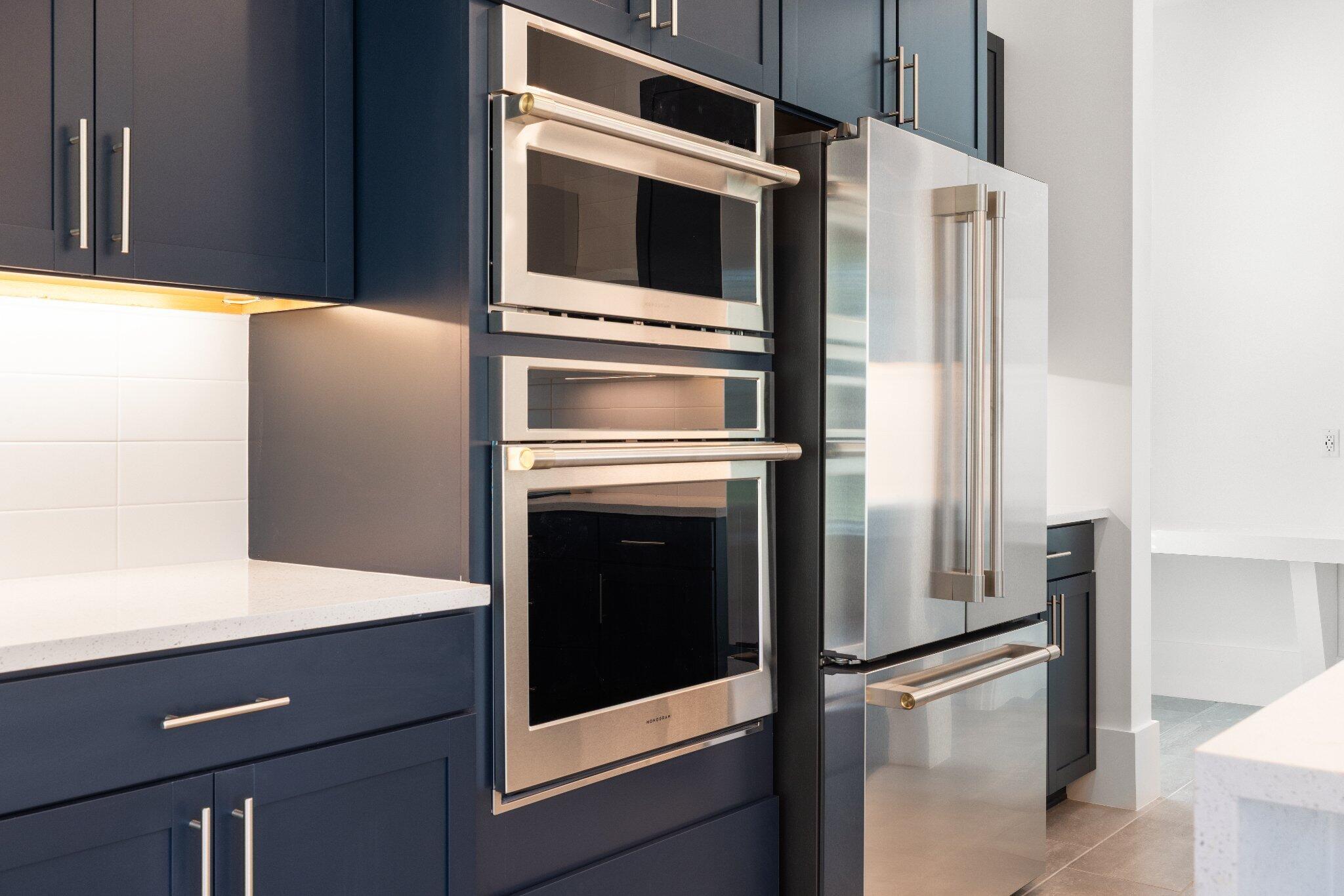 Deep blue shaker-style cabinetry featuring satin-finish hardware, stainless steel wall oven and microwave combination, stainless steel refrigerator, white tile backsplash, and solid-surface countertops