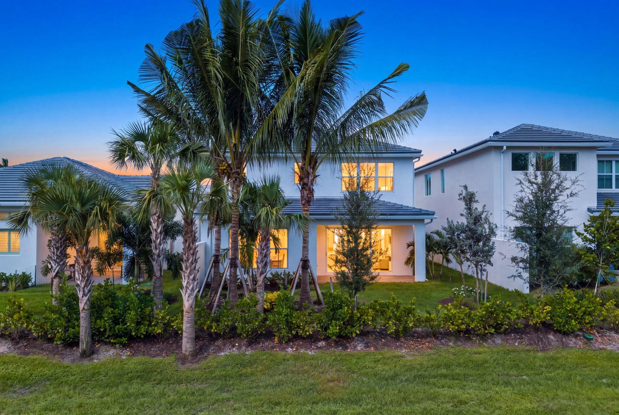 Two-story stucco exterior featuring a tiled roof, covered patio, lush palm tree landscaping, and a manicured lawn