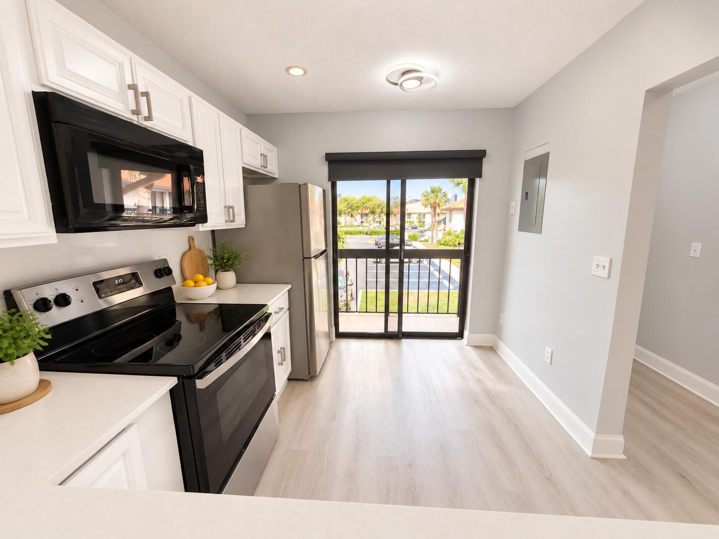 Kitchen featuring white shaker-style cabinetry, stainless steel appliances, solid-surface countertops, wood-finish flooring, and a sliding glass door with balcony access