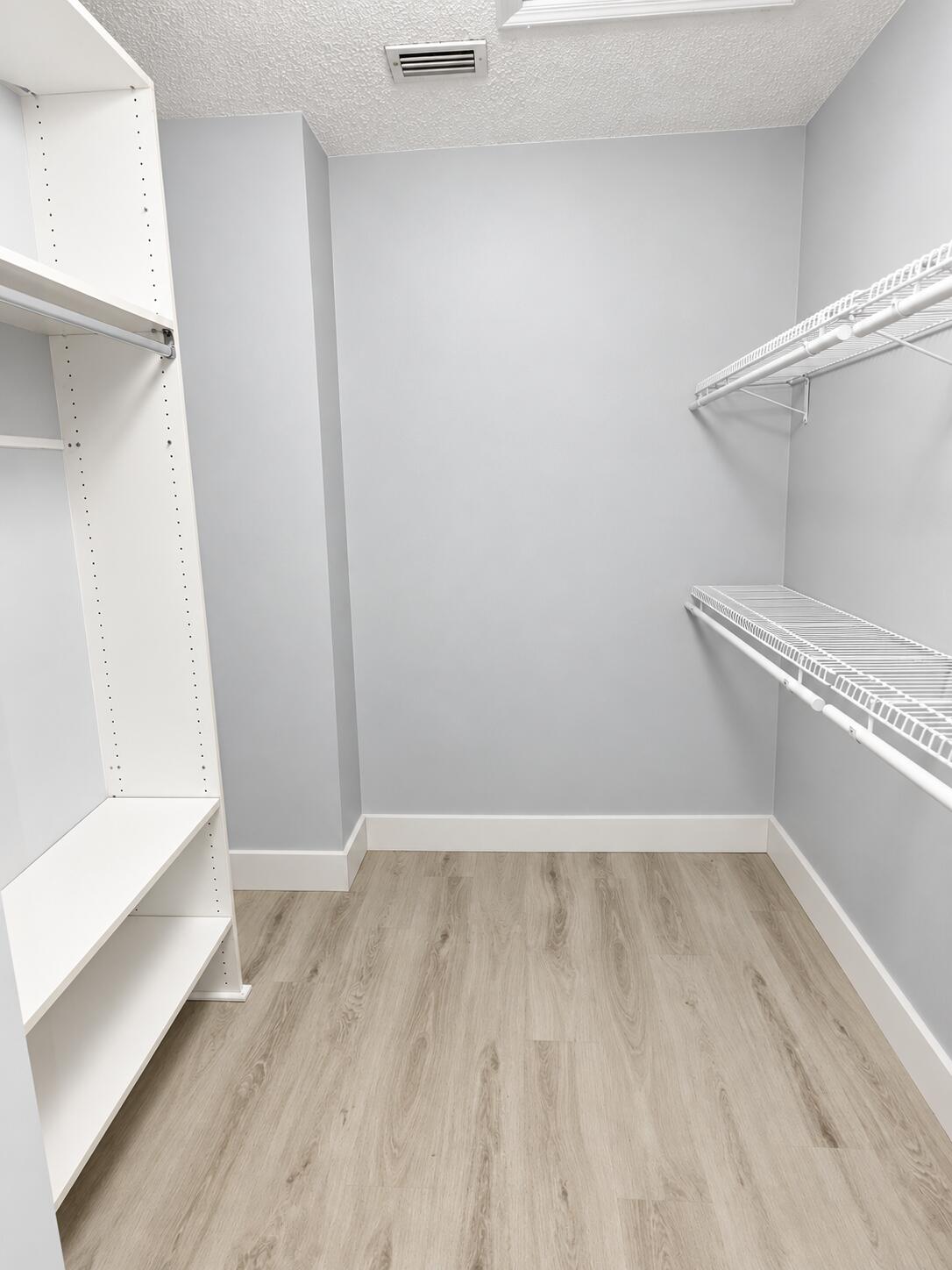 Walk-in closet featuring wood-finish flooring, white built-in shelving, and white wire rack shelving