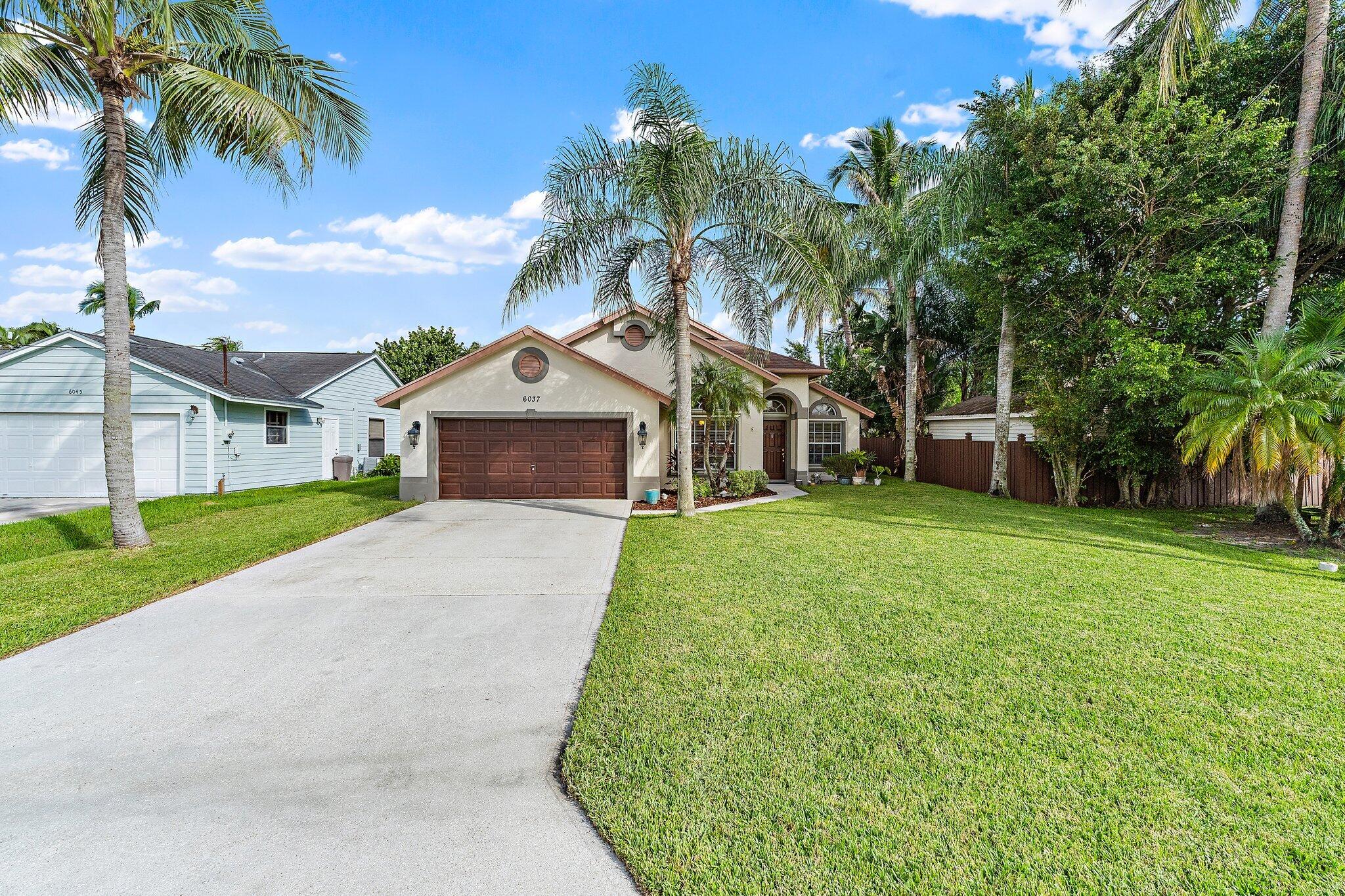 Front of the home from the street, with the driveway and mature palms.