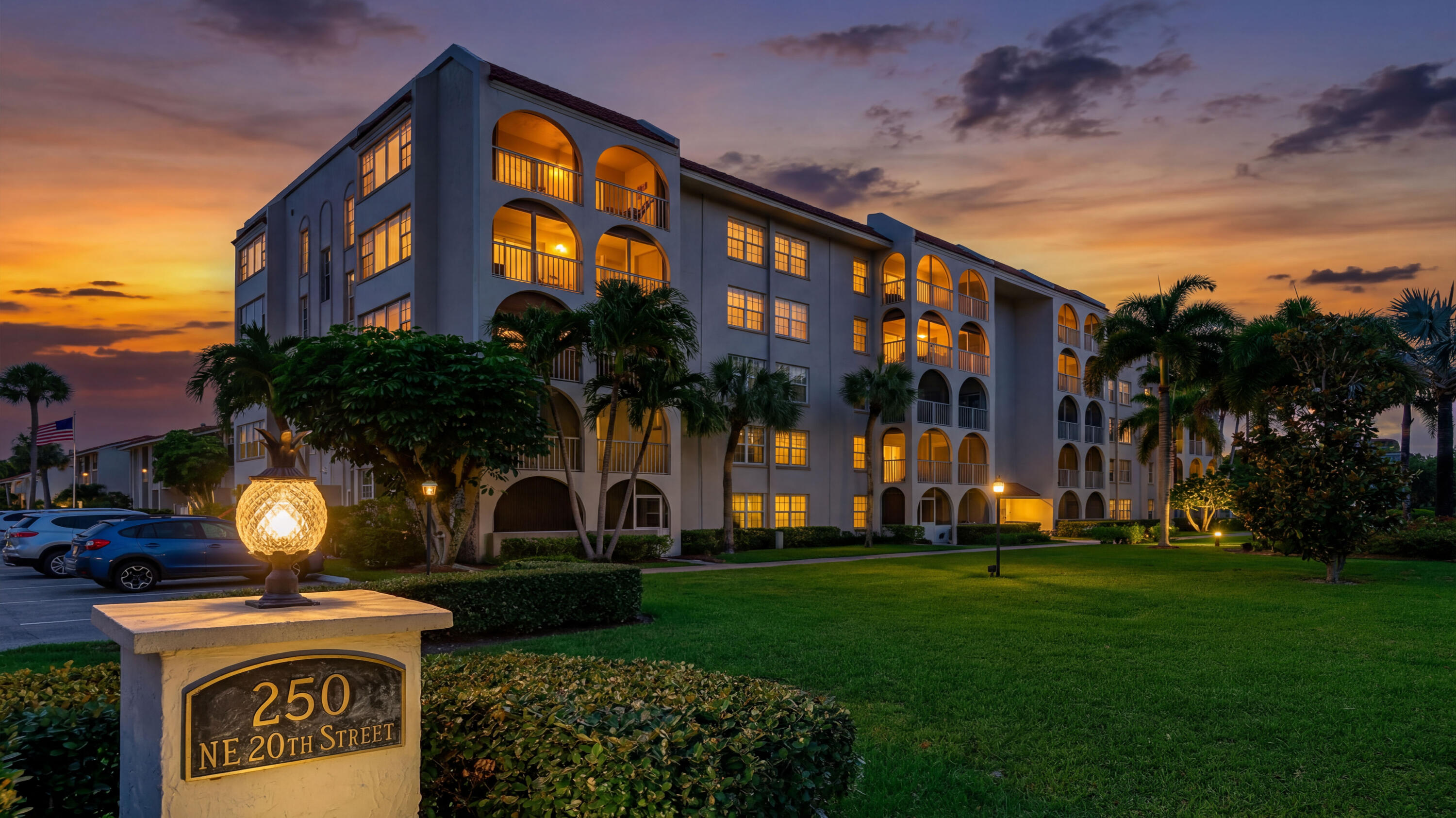 Multi-story residential building featuring arched private balconies, stucco exterior finish, mature palm trees, and manicured grounds