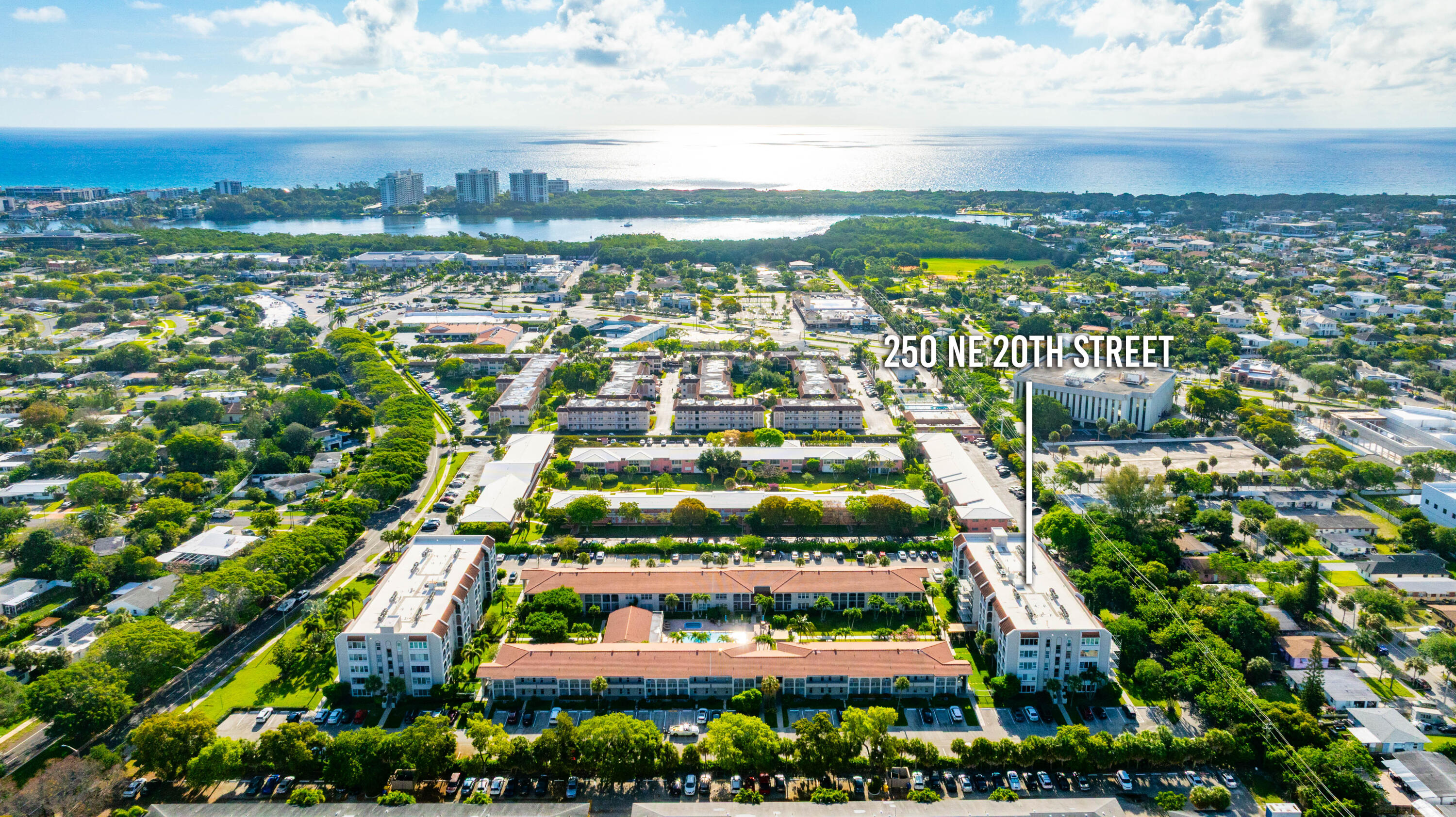 Aerial perspective of multi-story residential complex featuring terracotta-tiled roofs, central swimming pool, and mature landscaping