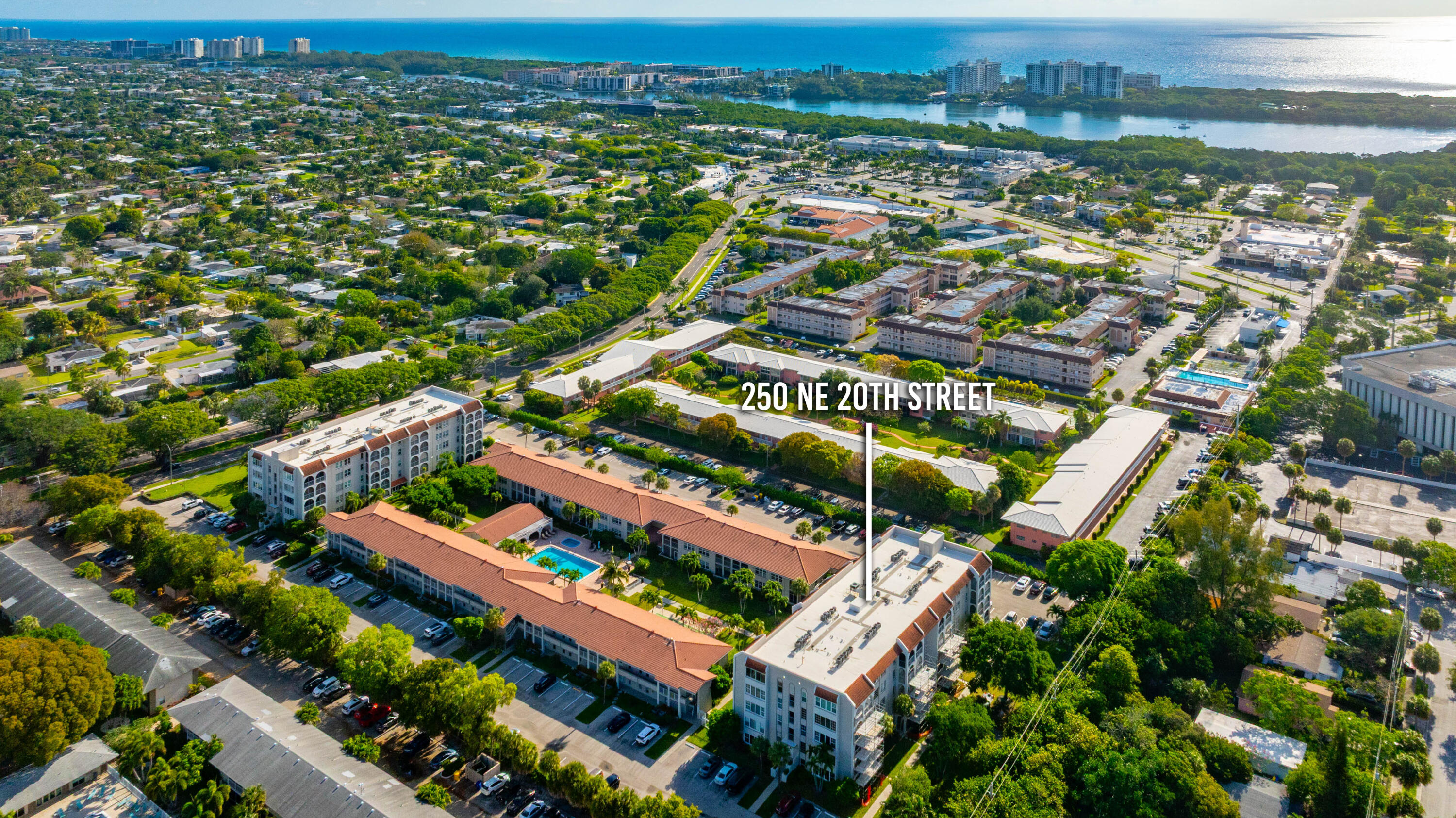 Aerial perspective of a multi-story residential complex featuring a central courtyard with an outdoor pool, paved parking areas, and mature landscaping