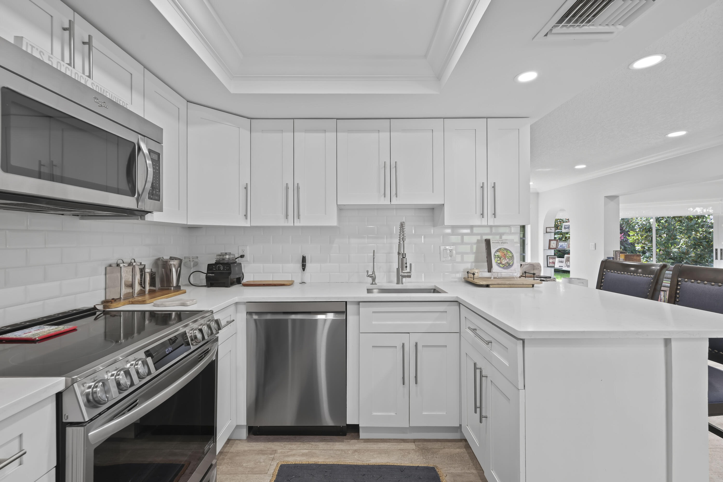 Kitchen featuring white Shaker-style cabinetry, stainless steel appliances, white subway tile backsplash, solid-surface countertops, and a tray ceiling with recessed lighting