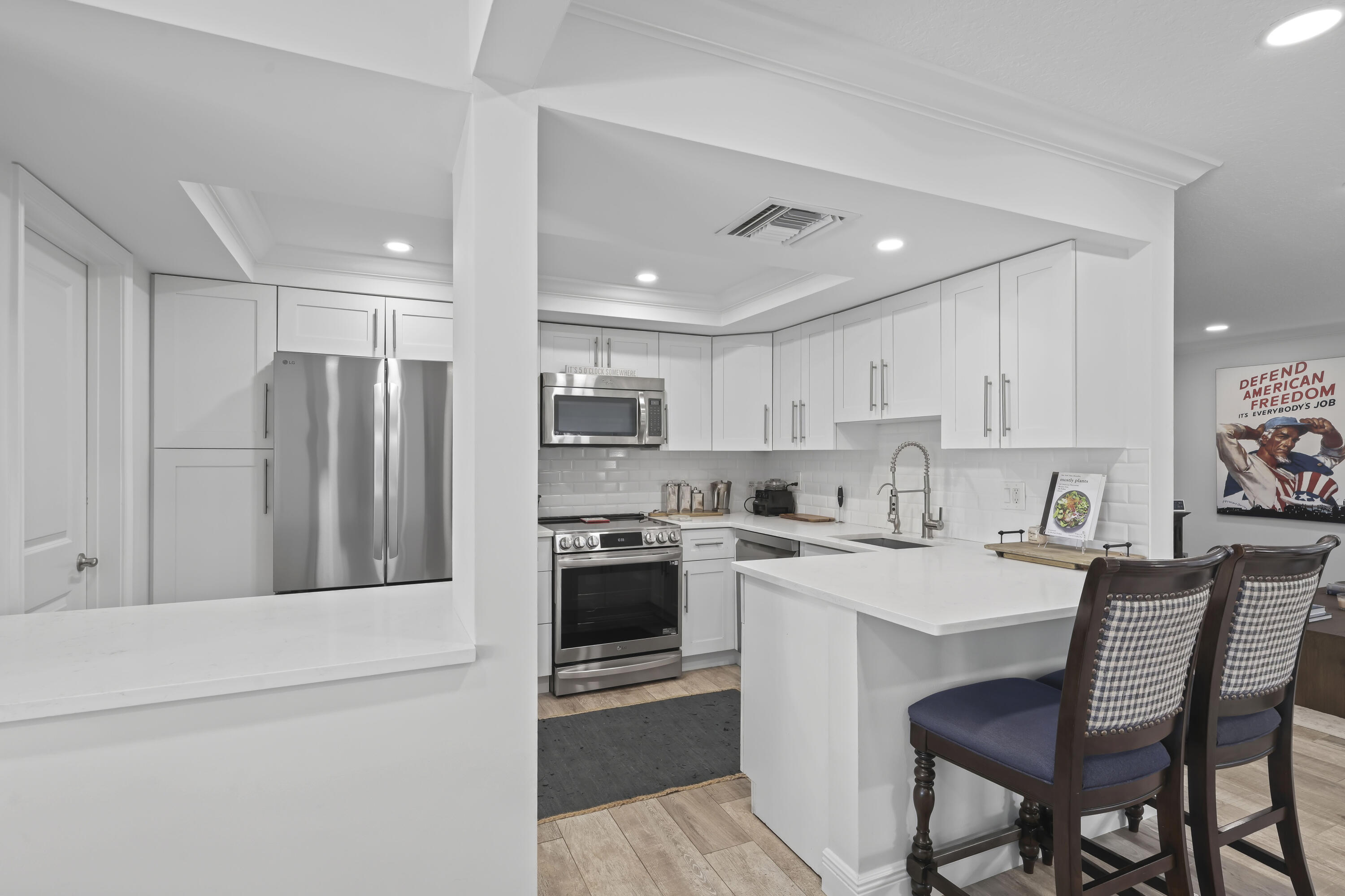 Kitchen featuring white cabinetry, quartz countertops, stainless steel appliances, a white subway tile backsplash, and wood-finish flooring