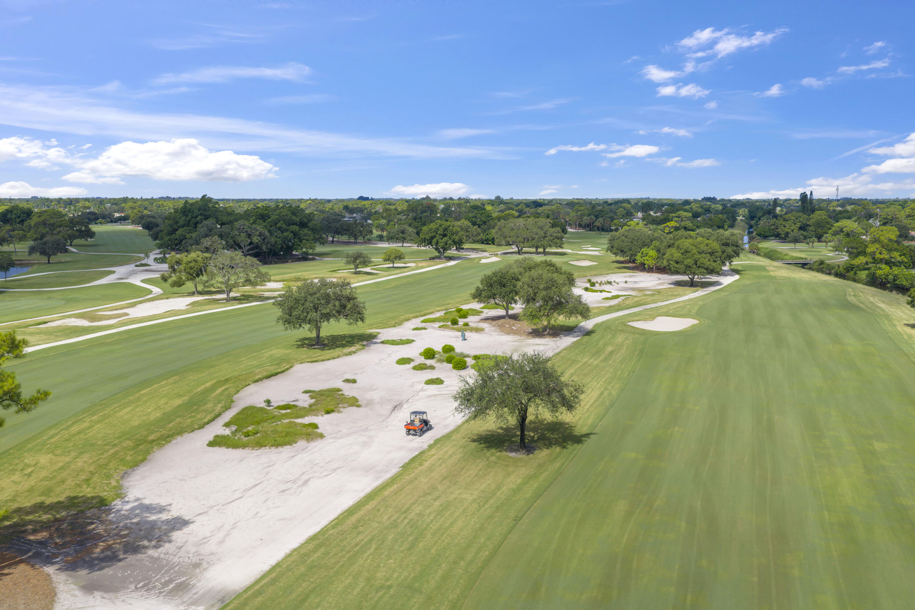 Aerial perspective of a golf course featuring expansive fairways, sand bunkers, mature trees, and manicured greens