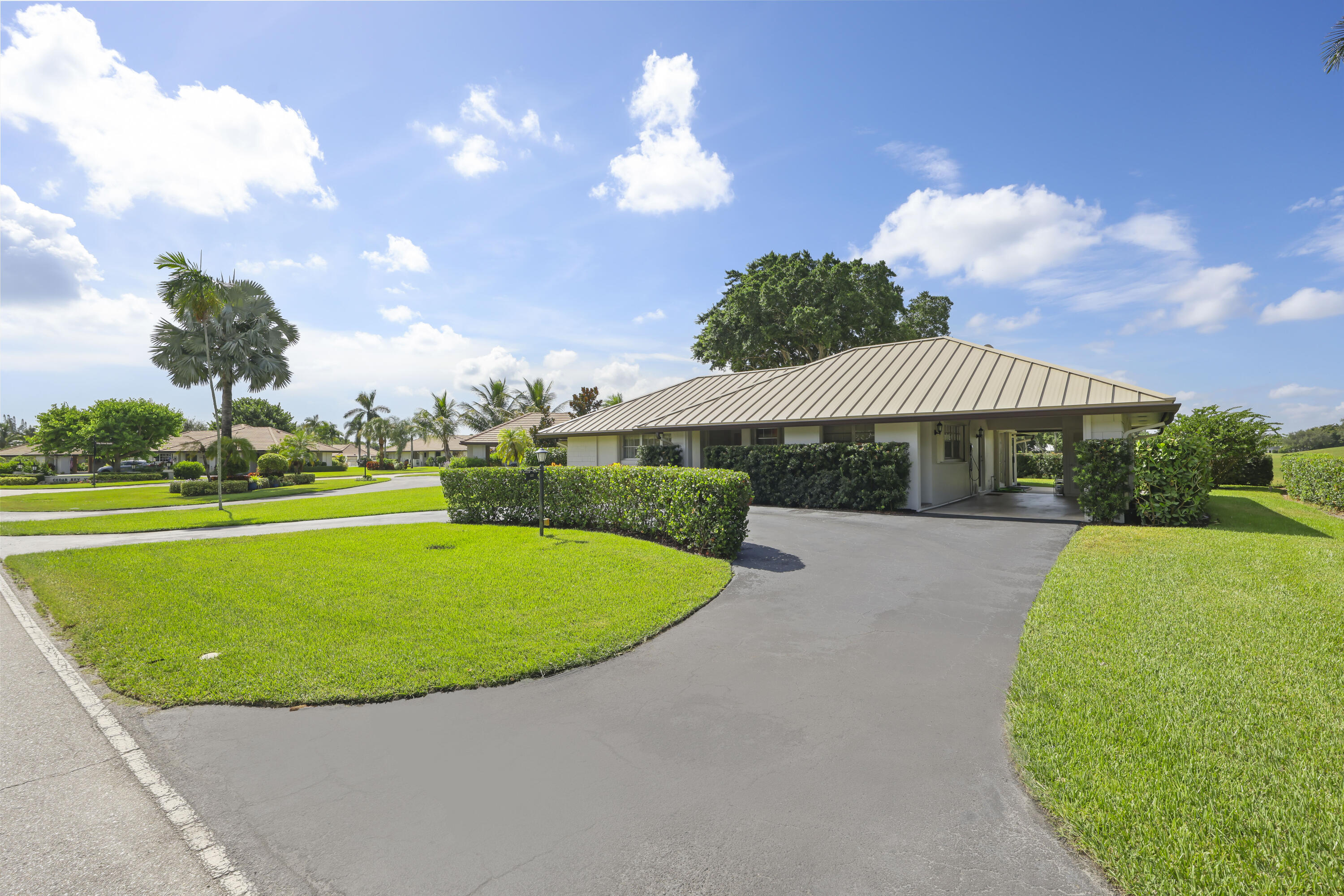 Single-story residence featuring a metal roof, attached carport, asphalt driveway, and manicured landscaping