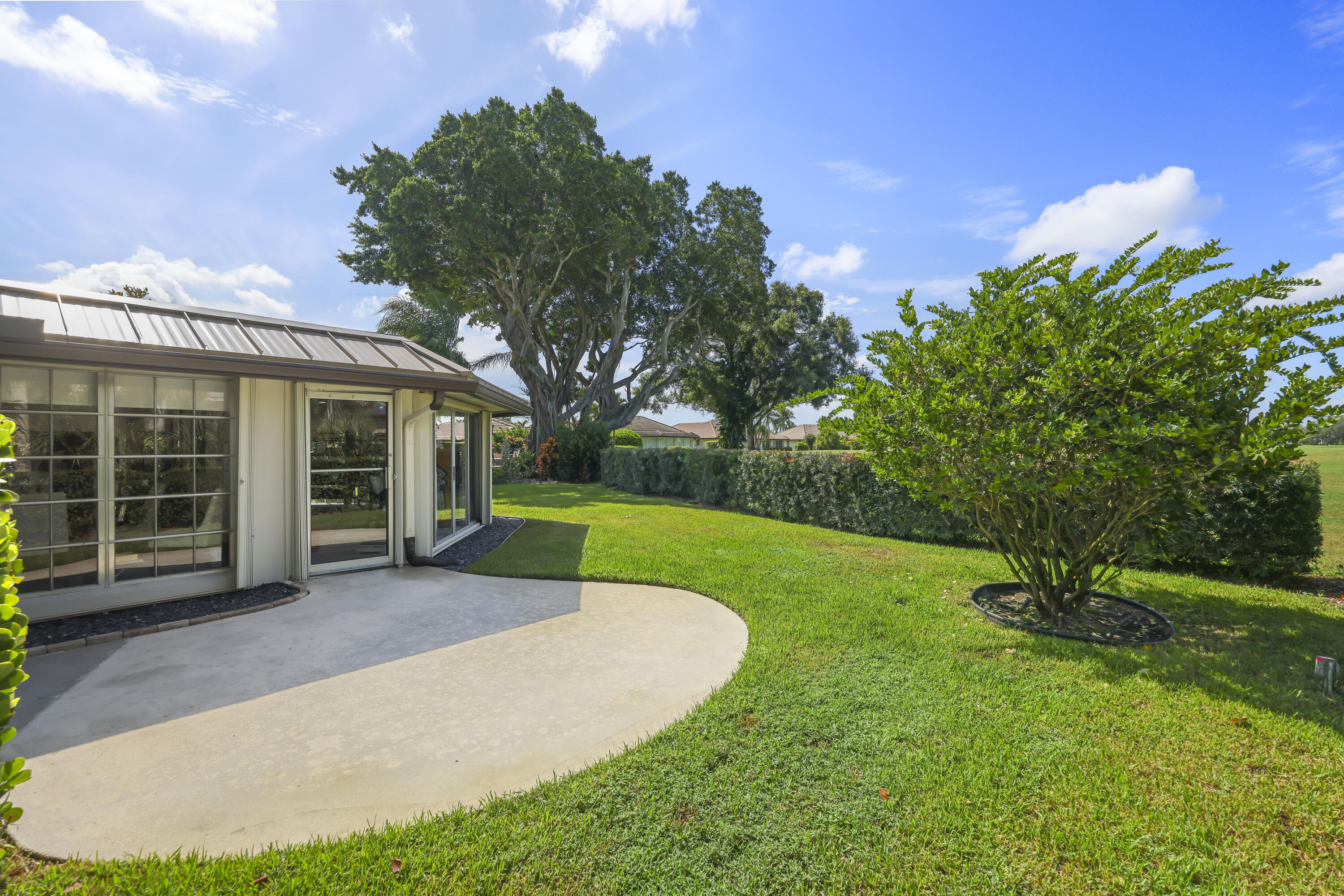 Rear exterior featuring a concrete patio, metal roofing, expansive manicured lawn, established landscaping, and mature trees