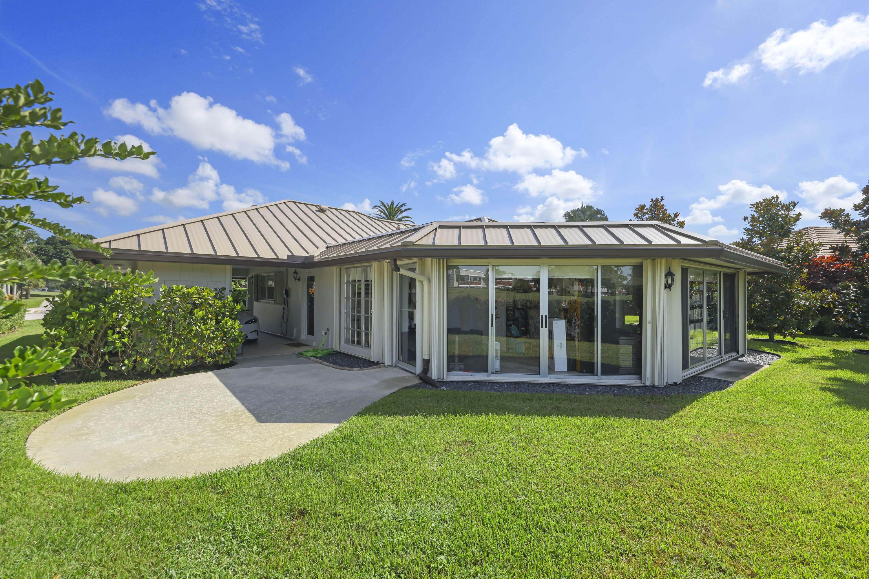 Single-story exterior featuring a metal roof, sliding glass wall panels, a concrete patio, and a grass lawn