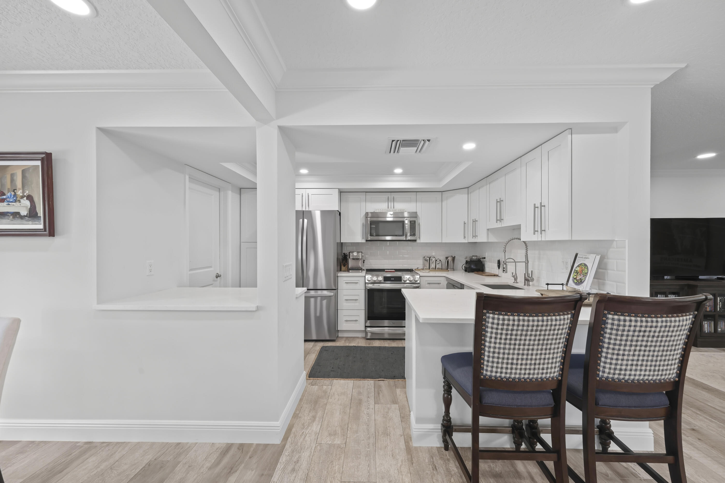 Kitchen featuring white shaker-style cabinetry, stainless steel appliances, white countertops, a subway tile backsplash, and wood-finish flooring