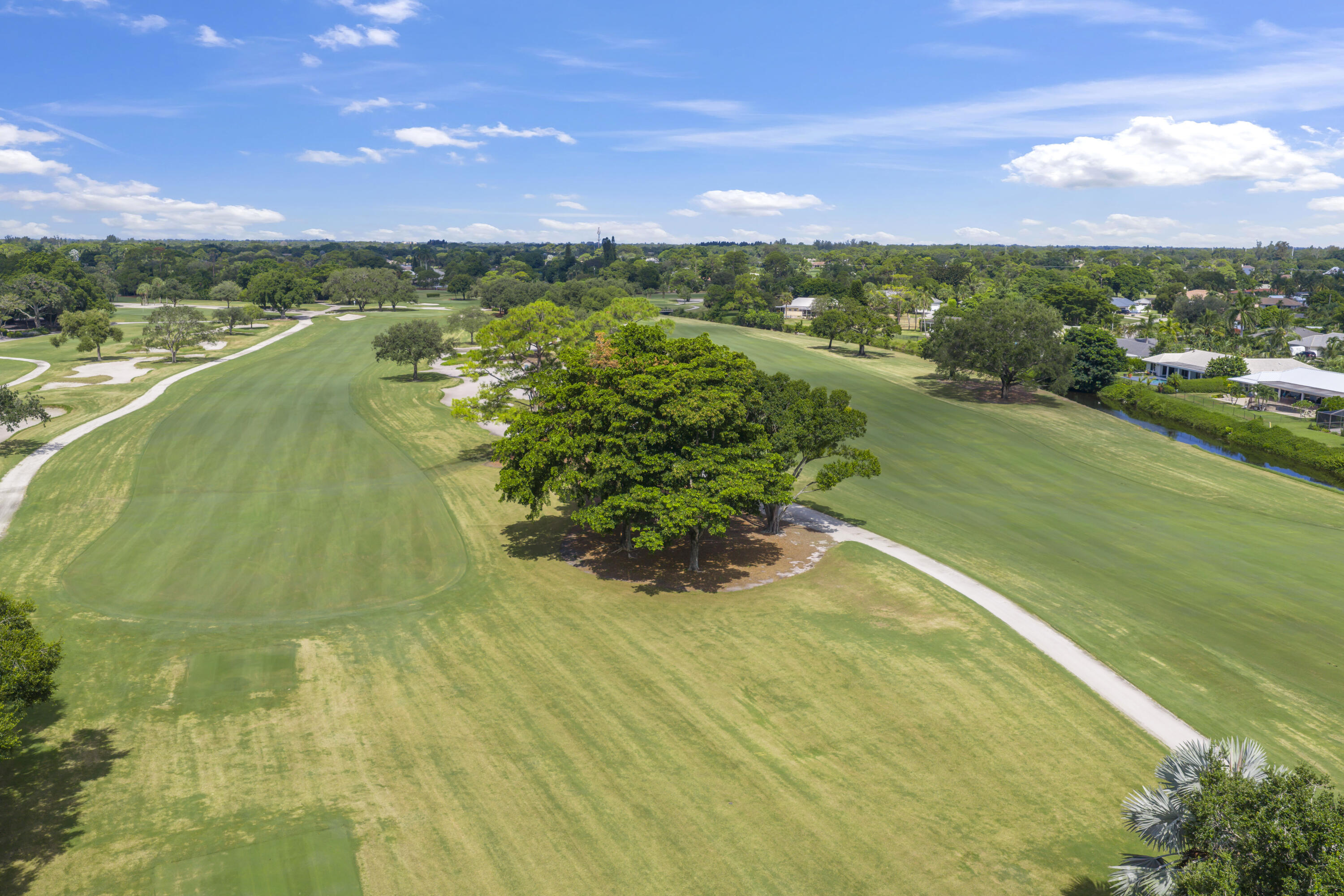 Aerial perspective of expansive golf course grounds featuring manicured fairways, mature canopy trees, concrete cart paths, and perimeter water frontage