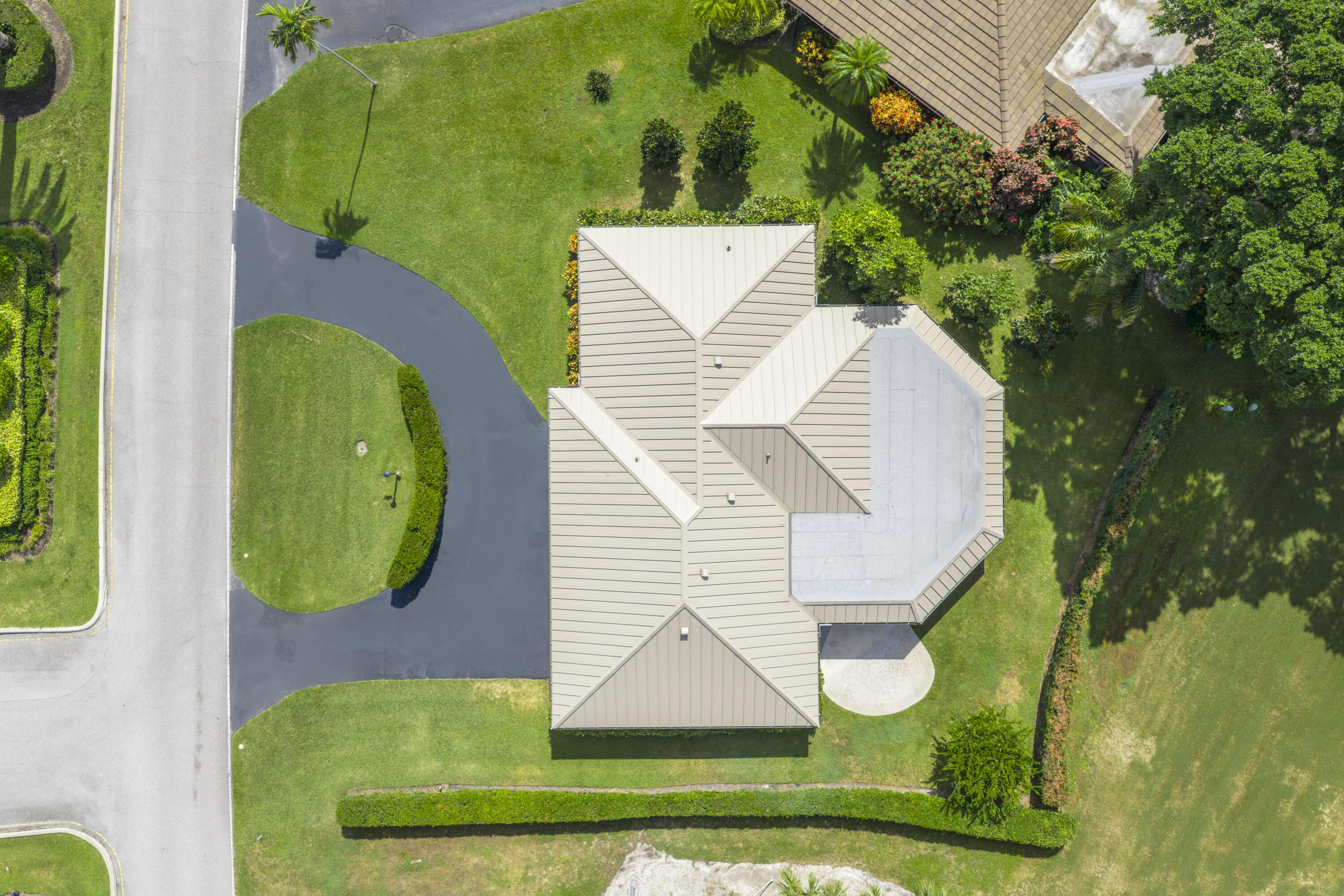 Aerial perspective of property featuring a metal roof, asphalt driveway, manicured landscaping, and mature trees