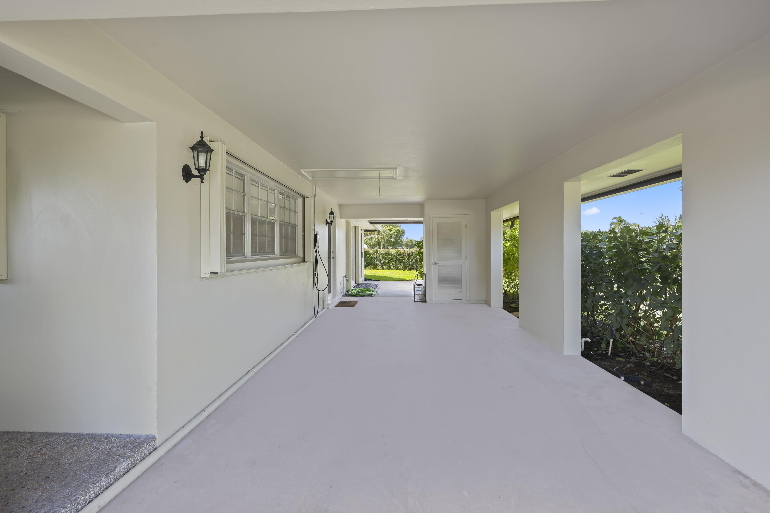 Covered carport featuring a concrete floor, exterior wall-mounted carriage lights, multi-pane window, and integrated storage door