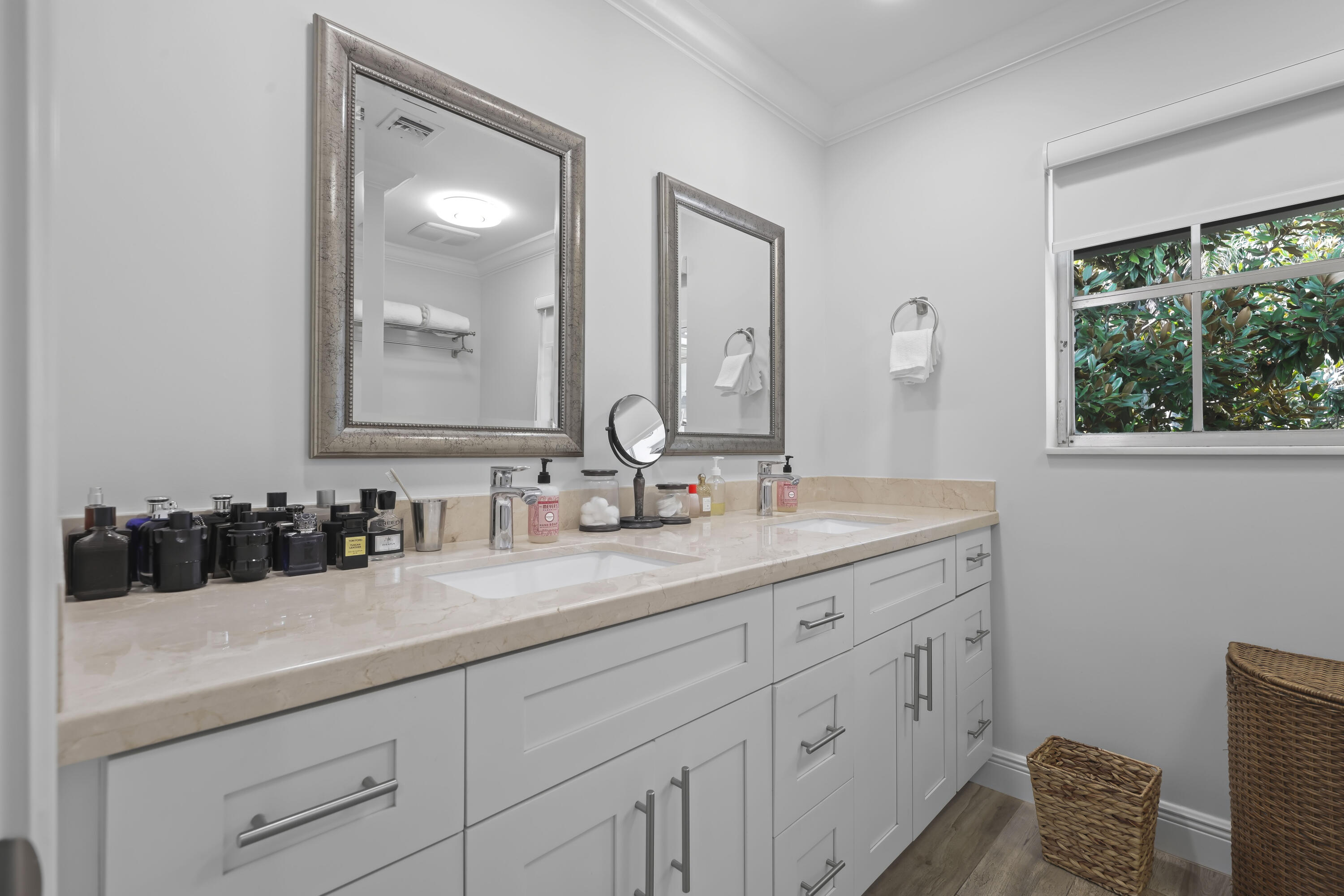 Double vanity featuring a light-toned stone countertop, dual undermount sinks, custom white cabinetry with brushed nickel hardware, and framed mirrors