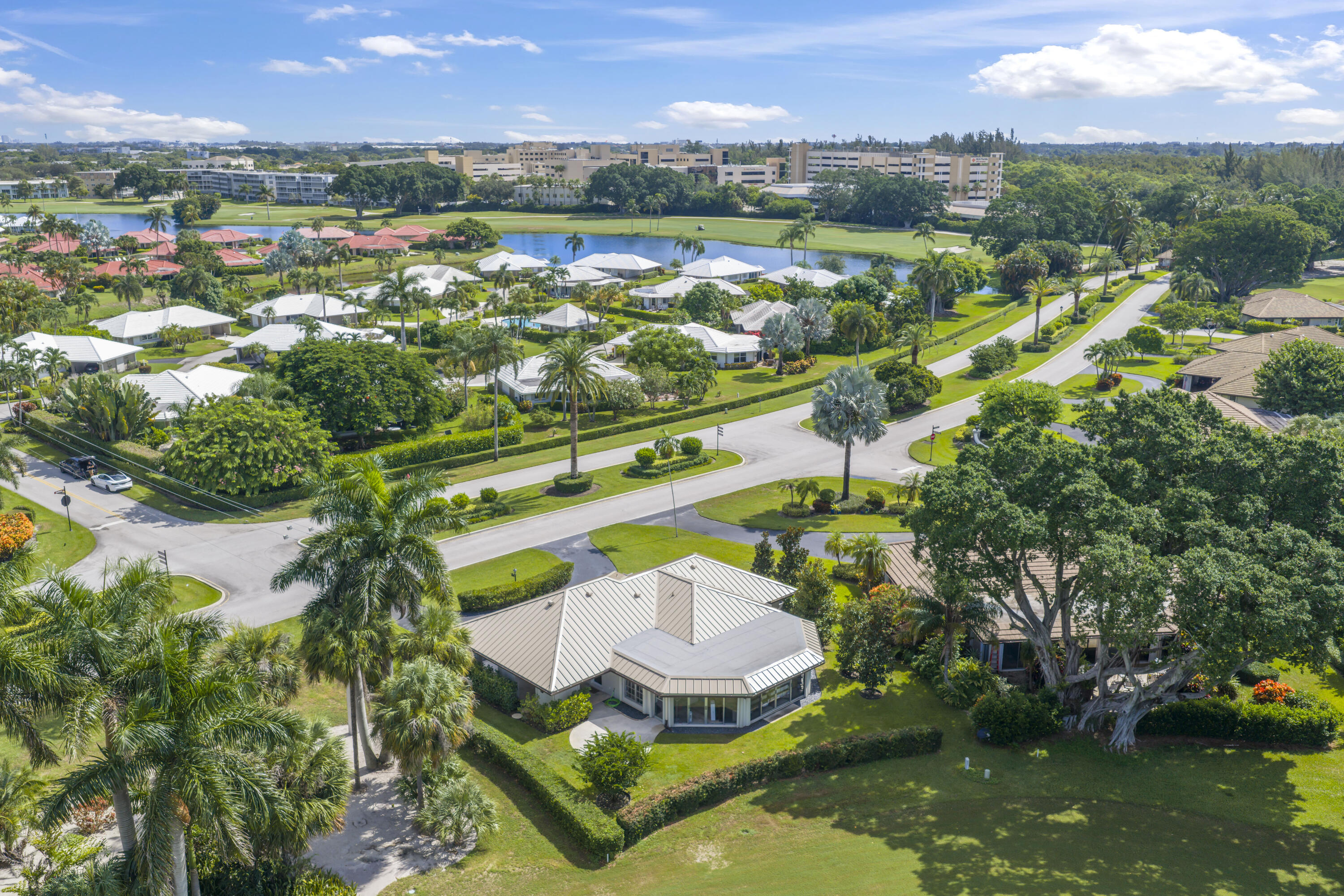 Aerial perspective featuring a single-story residence with a metal roof, situated on a landscaped lot with mature palm trees and expansive lawns