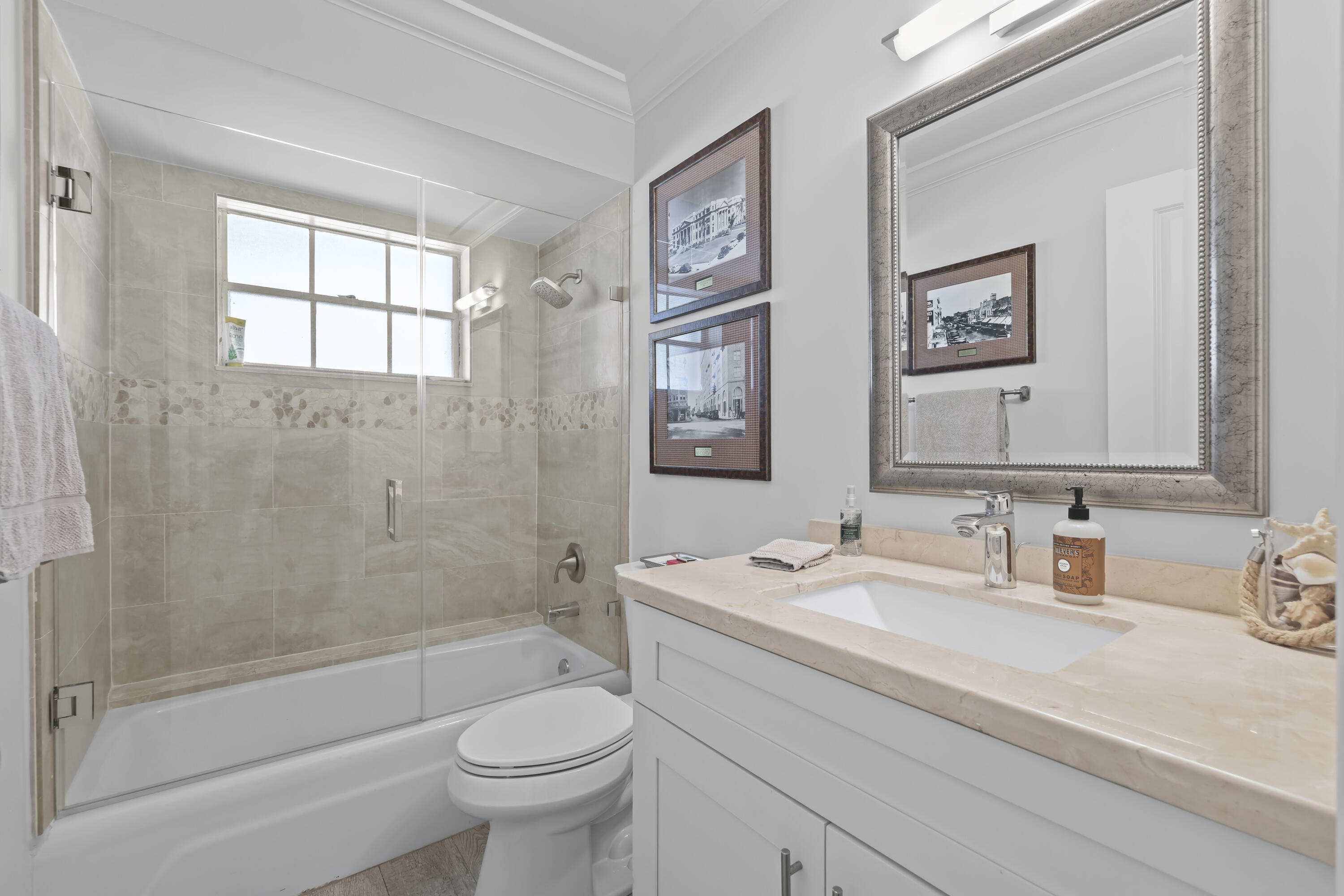 Bathroom featuring a white vanity with a stone countertop, an integrated rectangular sink, a shower-tub combination with a glass door enclosure, and a wall-mounted mirror