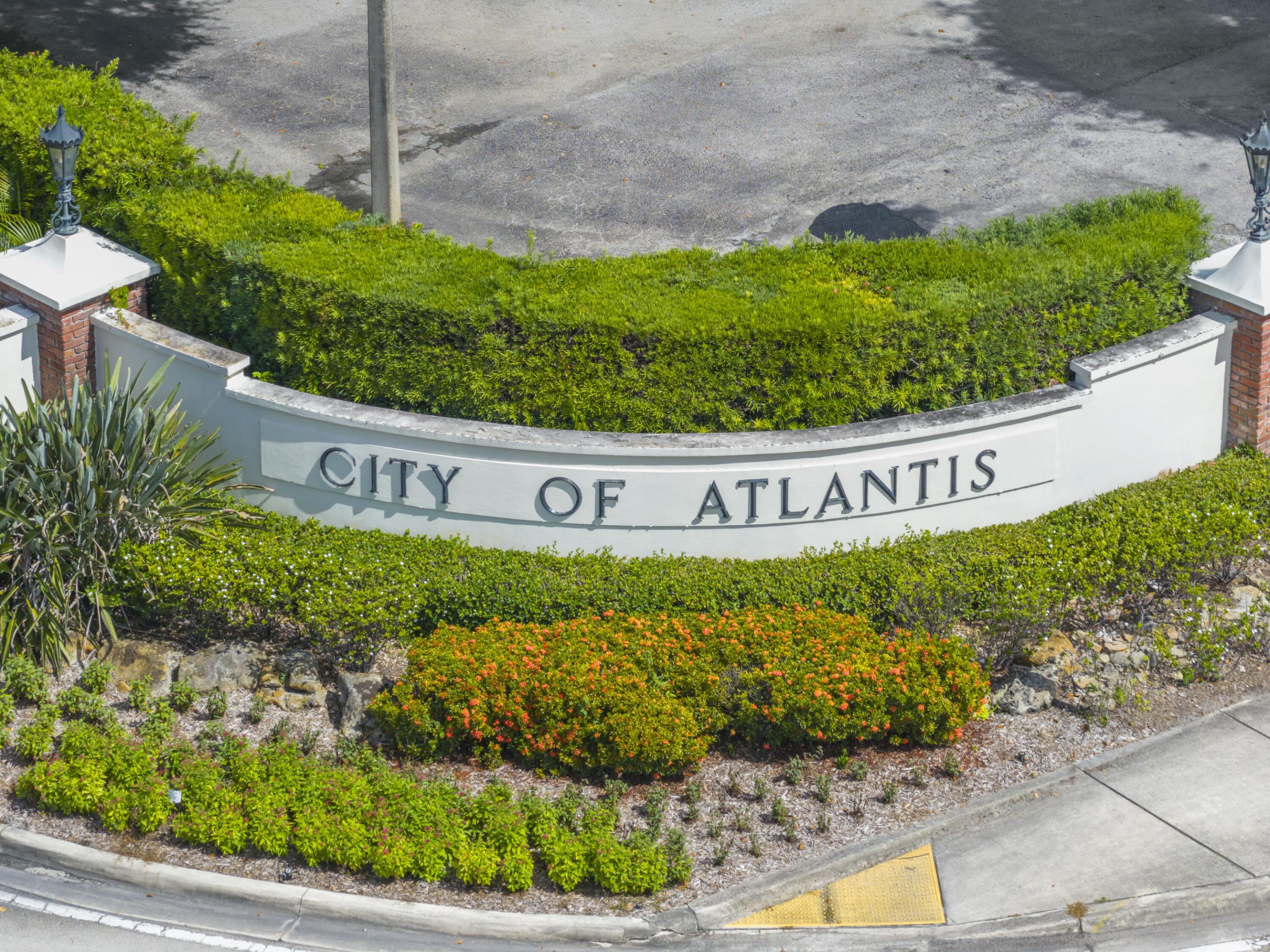 Curved masonry signage with brick pillar accents, integrated lighting fixtures, and professional landscaping featuring manicured hedges and ornamental shrubs