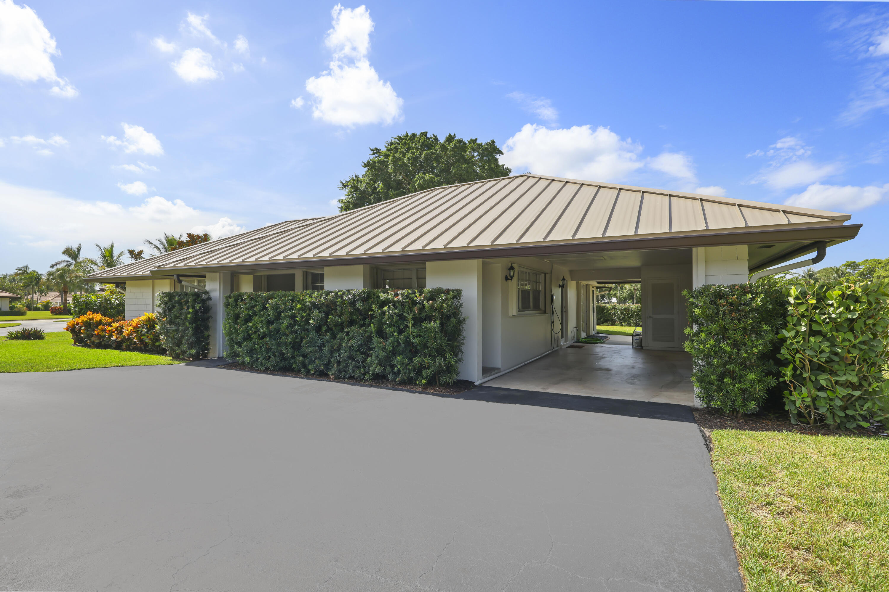 Single-story exterior featuring a standing-seam metal roof, integrated carport, paved driveway, and manicured landscaping