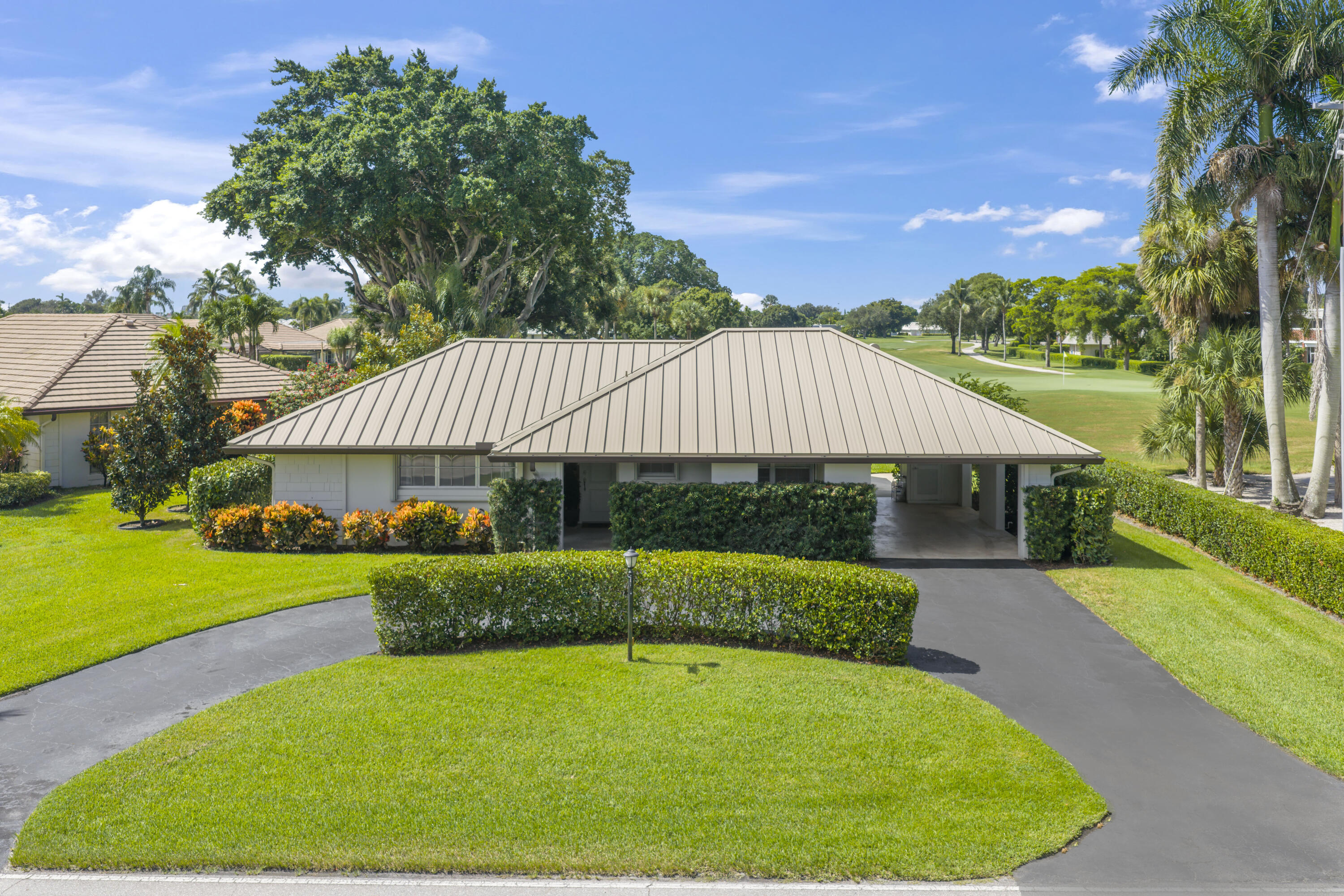 Single-story residence featuring a standing-seam metal roof, attached carport, paved circular driveway, and manicured landscaping