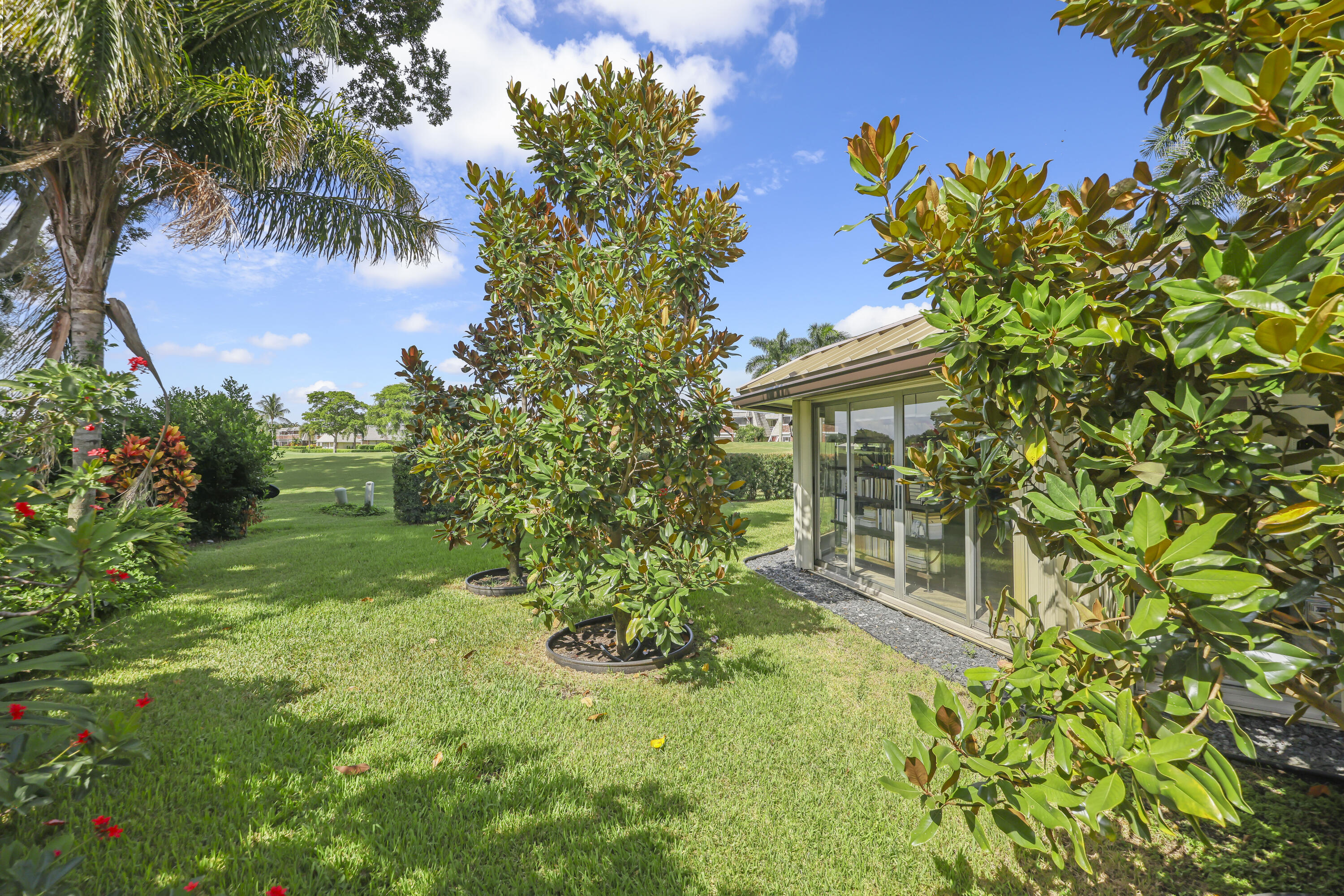 Expansive lawn with mature landscaping, including established trees and shrubs, featuring a structural exterior with floor-to-ceiling sliding glass doors and gravel perimeter accent