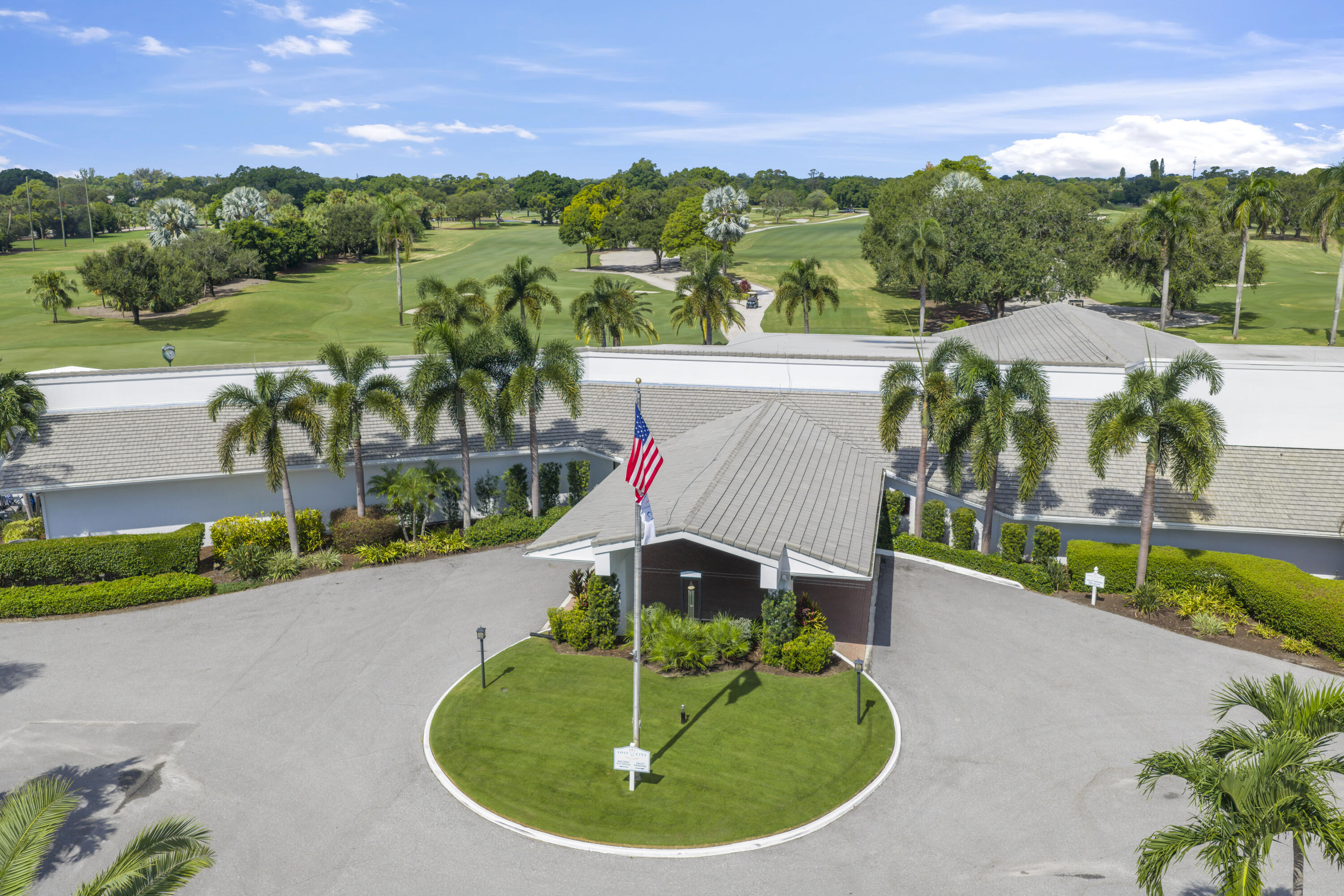 Asphalt porte-cochre entrance with a circular driveway and manicured lawn roundabout, featuring a metal roofline and professional landscaping