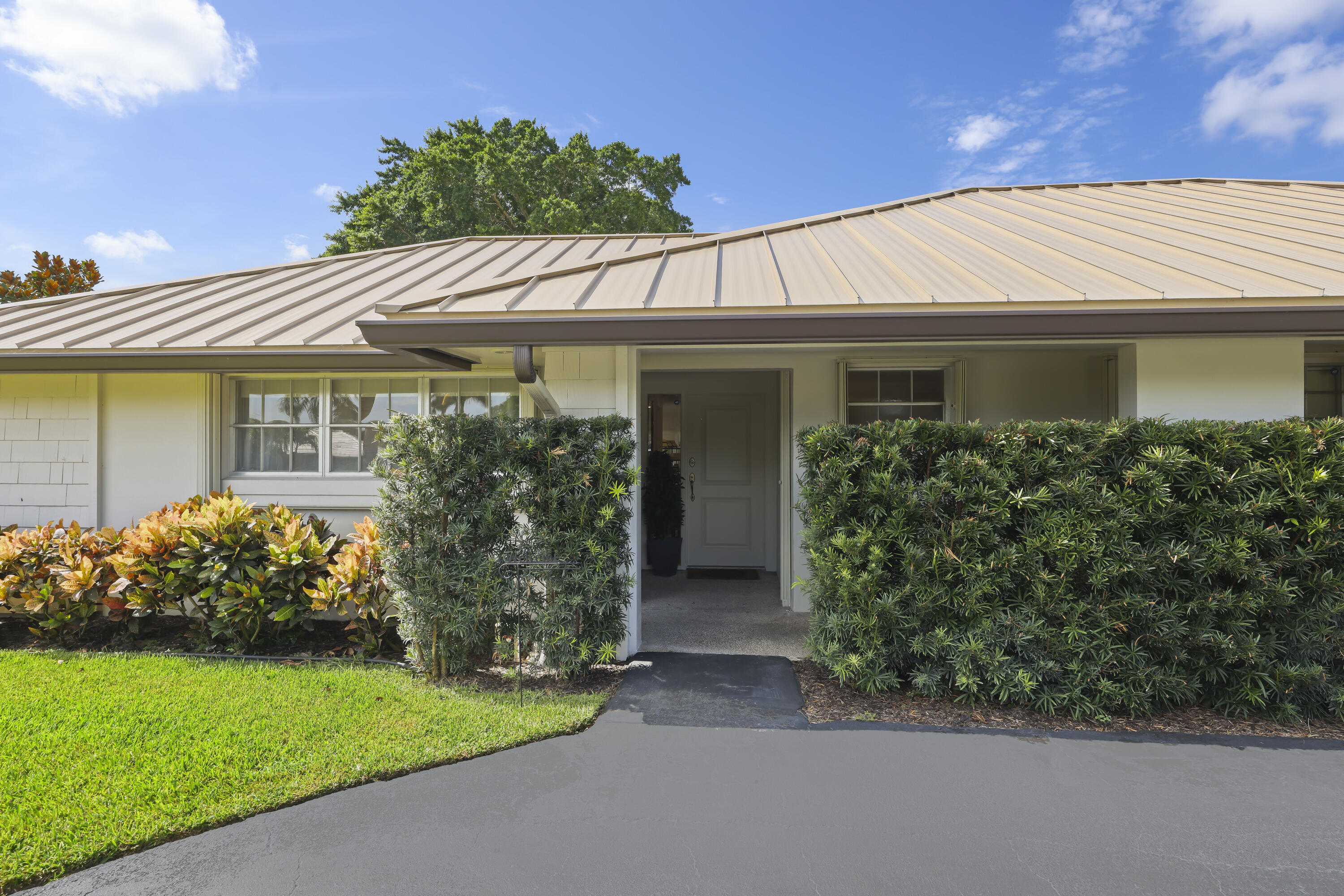 Exterior facade featuring a standing-seam metal roof, crisp white masonry walls, a recessed entryway, and manicured shrubbery