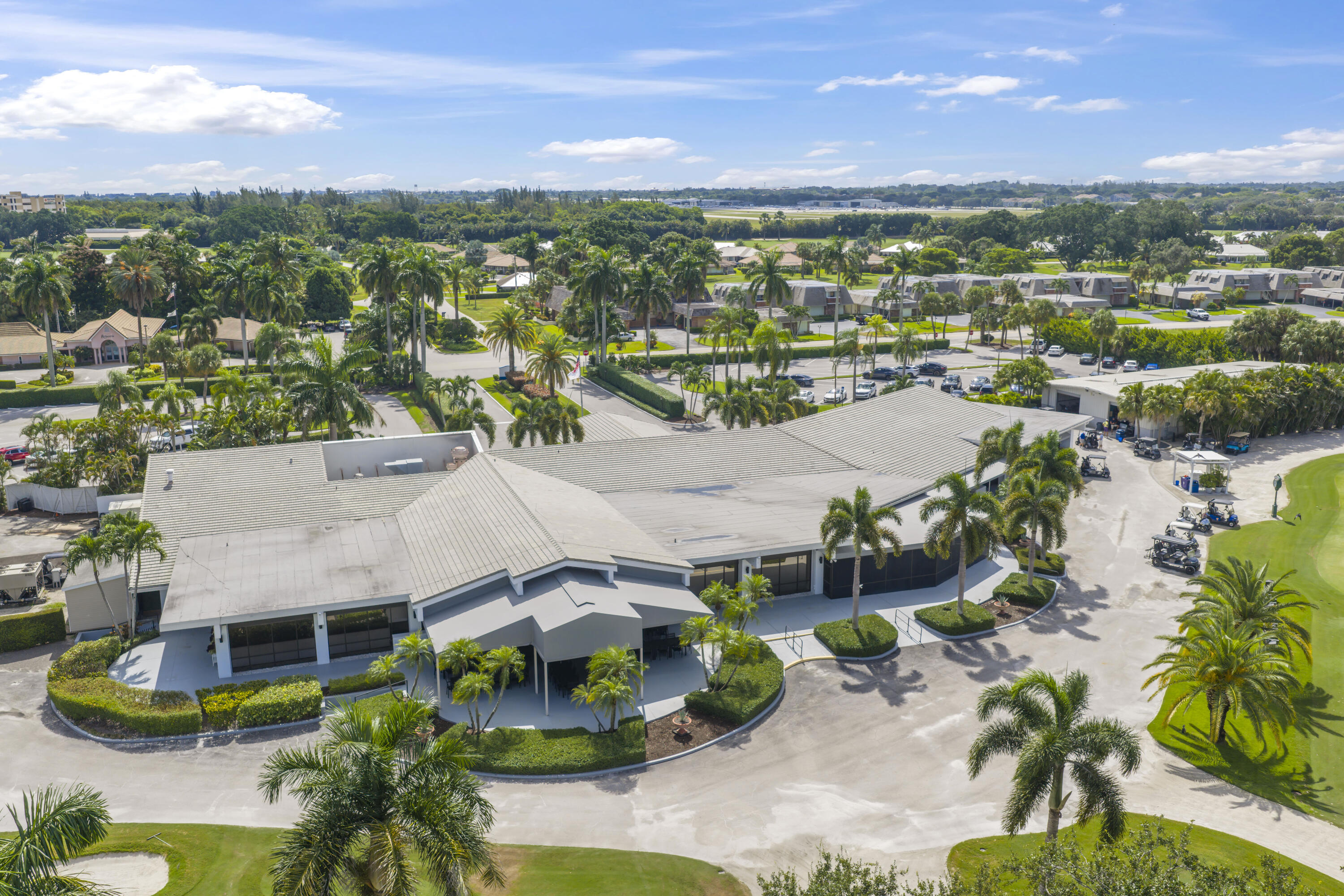 Aerial view of a sprawling clubhouse featuring a multi-gabled roof, covered entrance portico, and direct course-side positioning